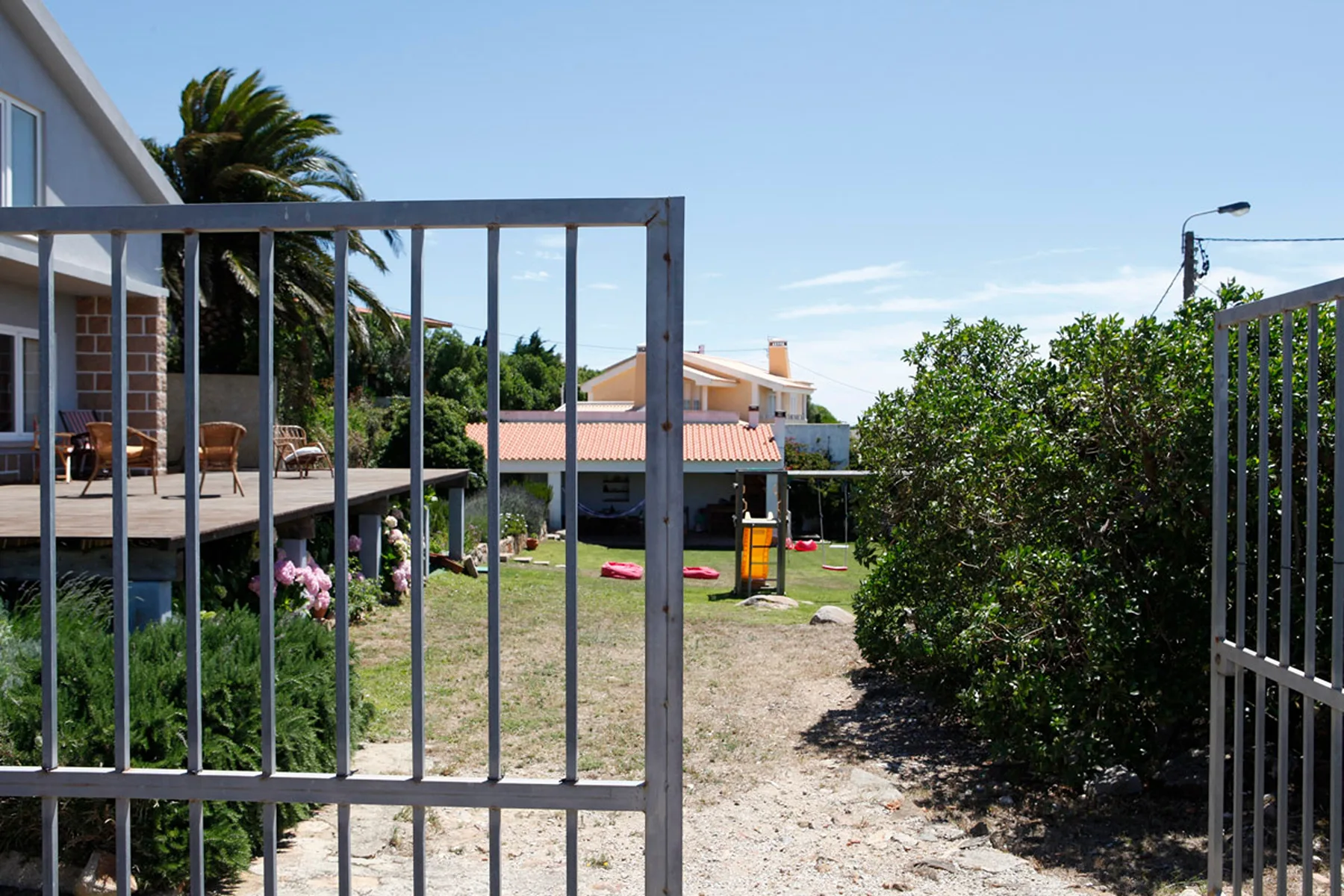A garden path runs between a metal gate and shrubs toward a house.