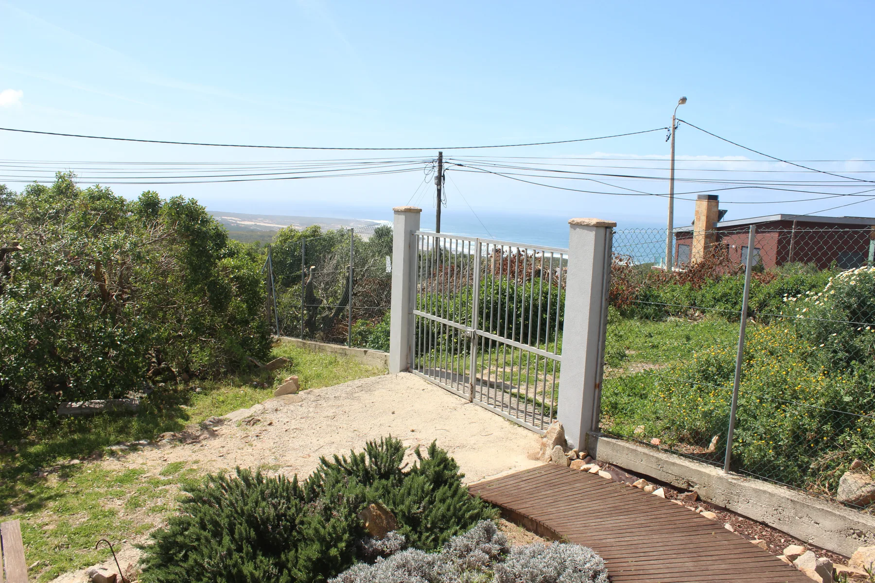 A garden path leads to a metal gate, with the sea visible in the distance.