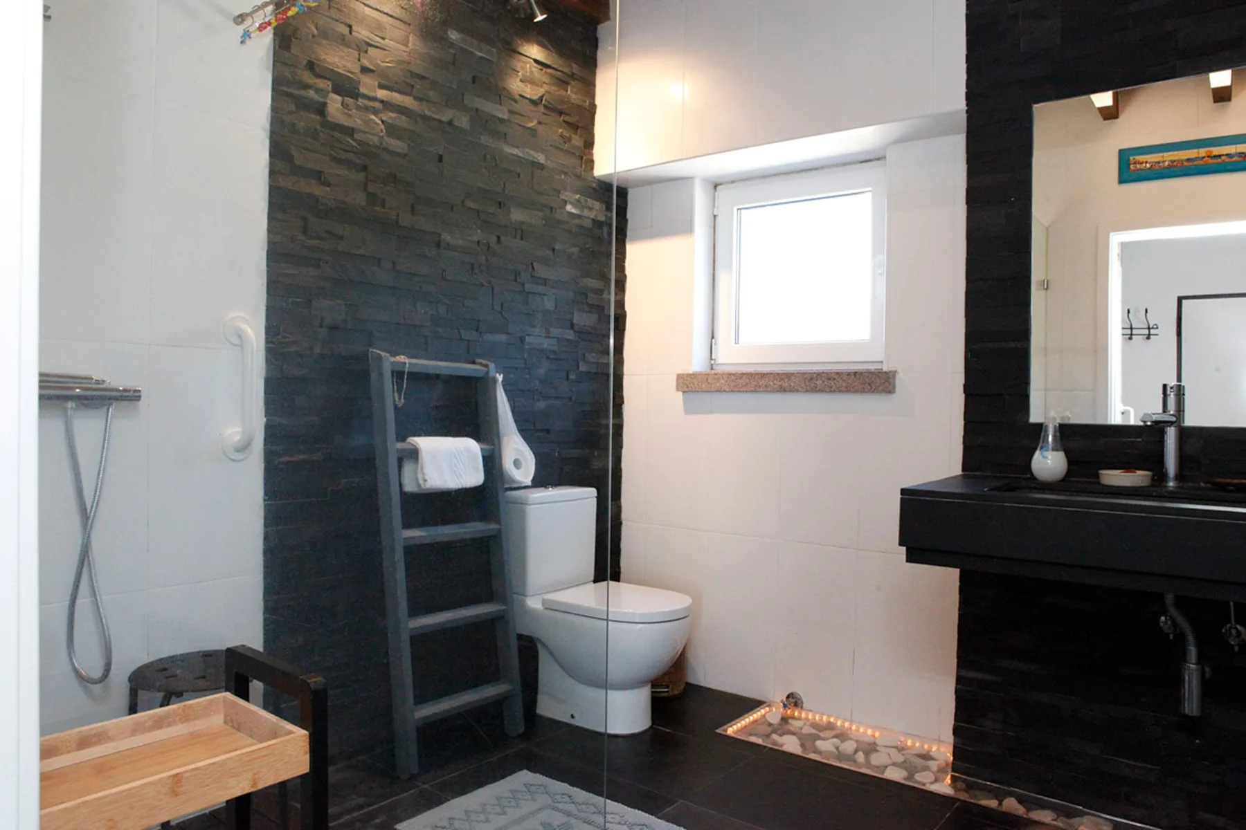 A bathroom with a toilet, shower, and dark stone accent wall.
