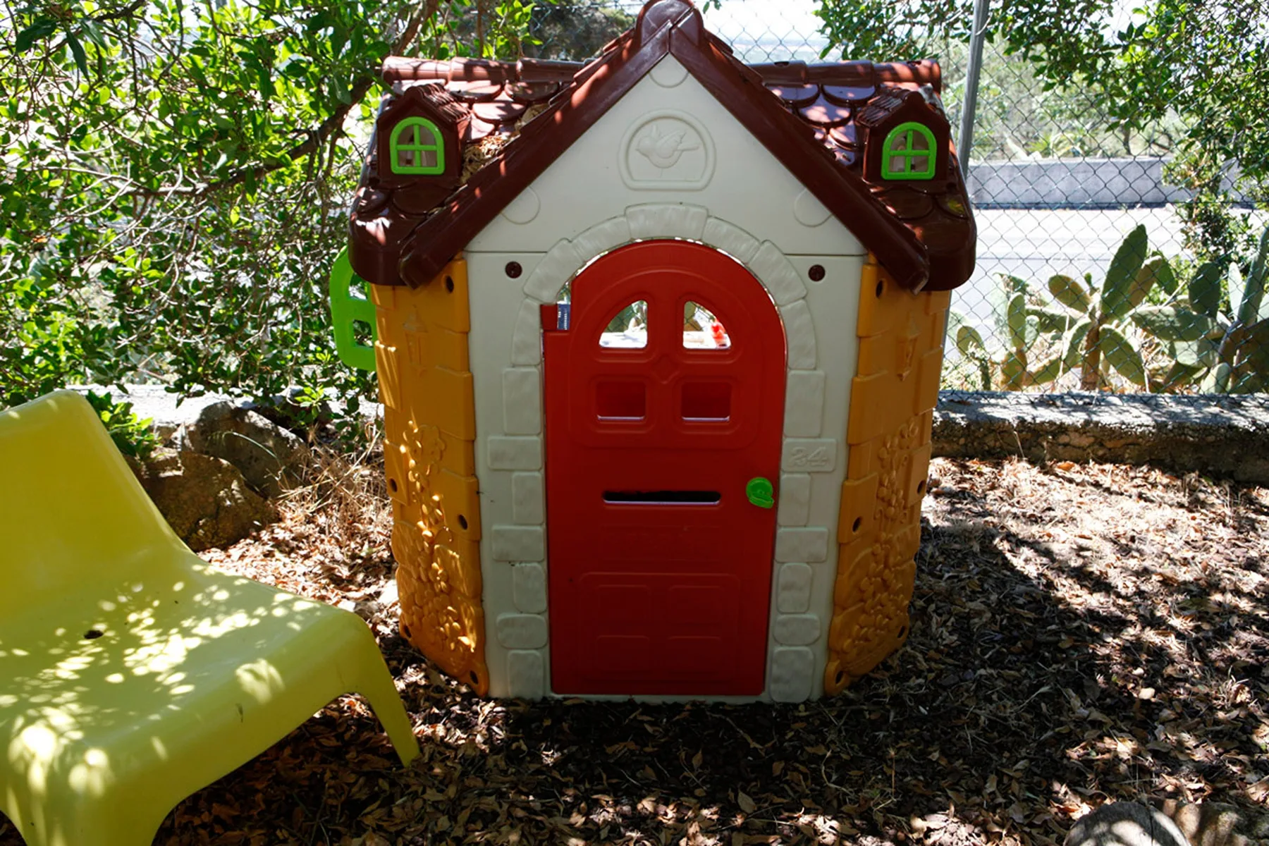 A small children's playhouse stands among trees and leafy ground cover.