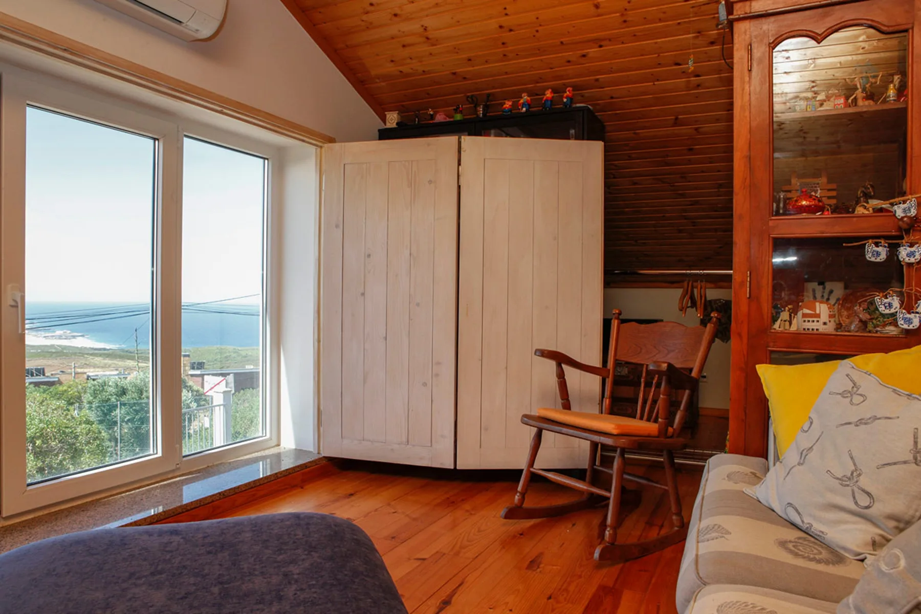 A wood-paneled living room with seating beside large windows overlooking the coast.