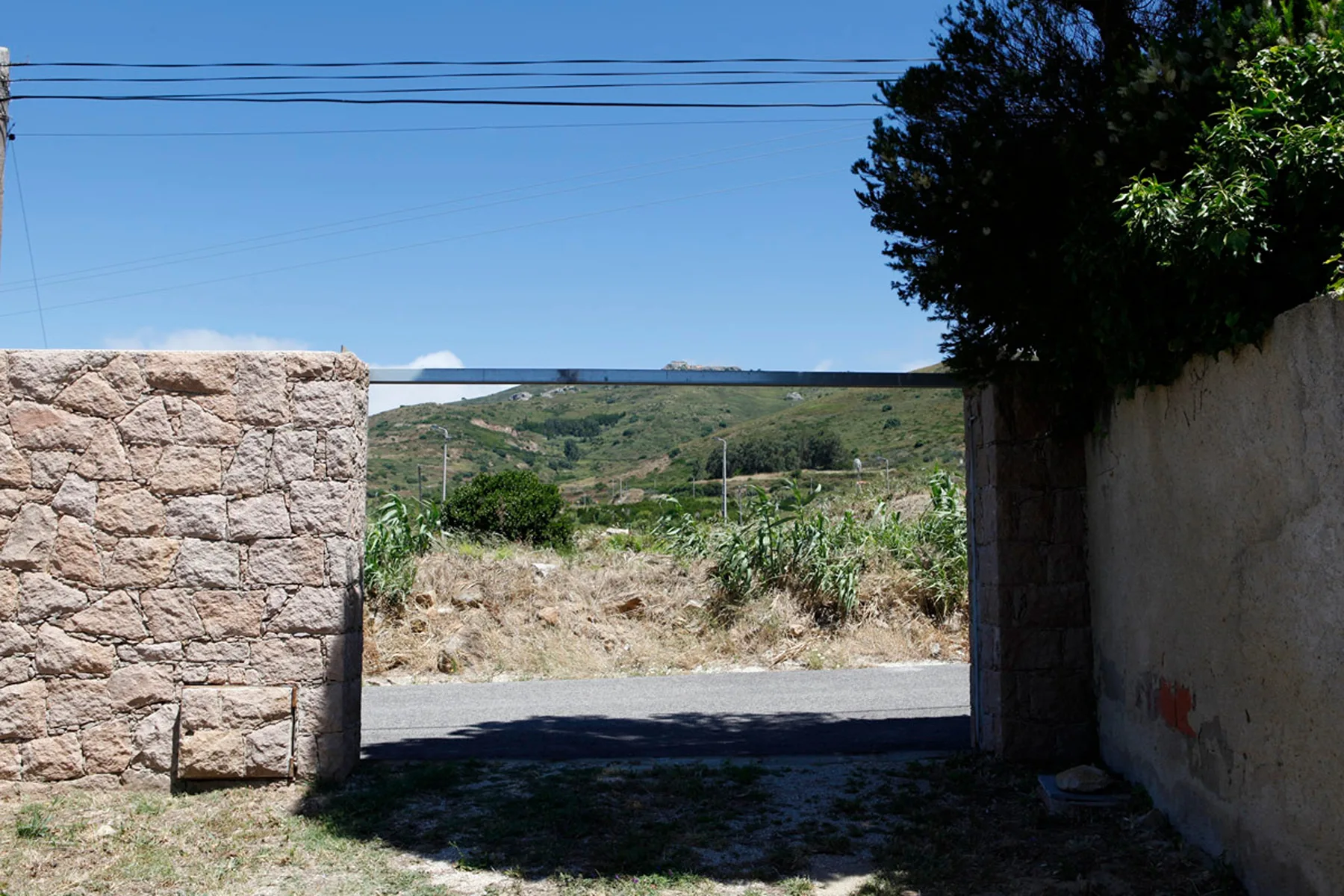 An outdoor entrance opens onto a road and green hills beneath a clear sky.