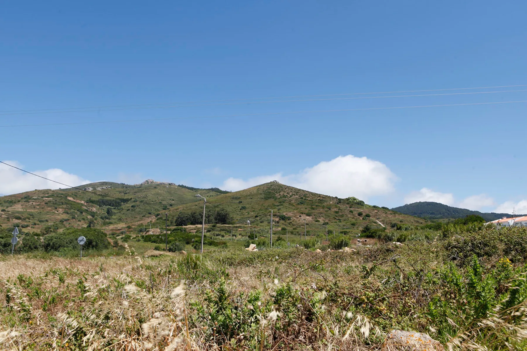 A wide open landscape of scrubby fields and green hills beneath a clear blue sky.