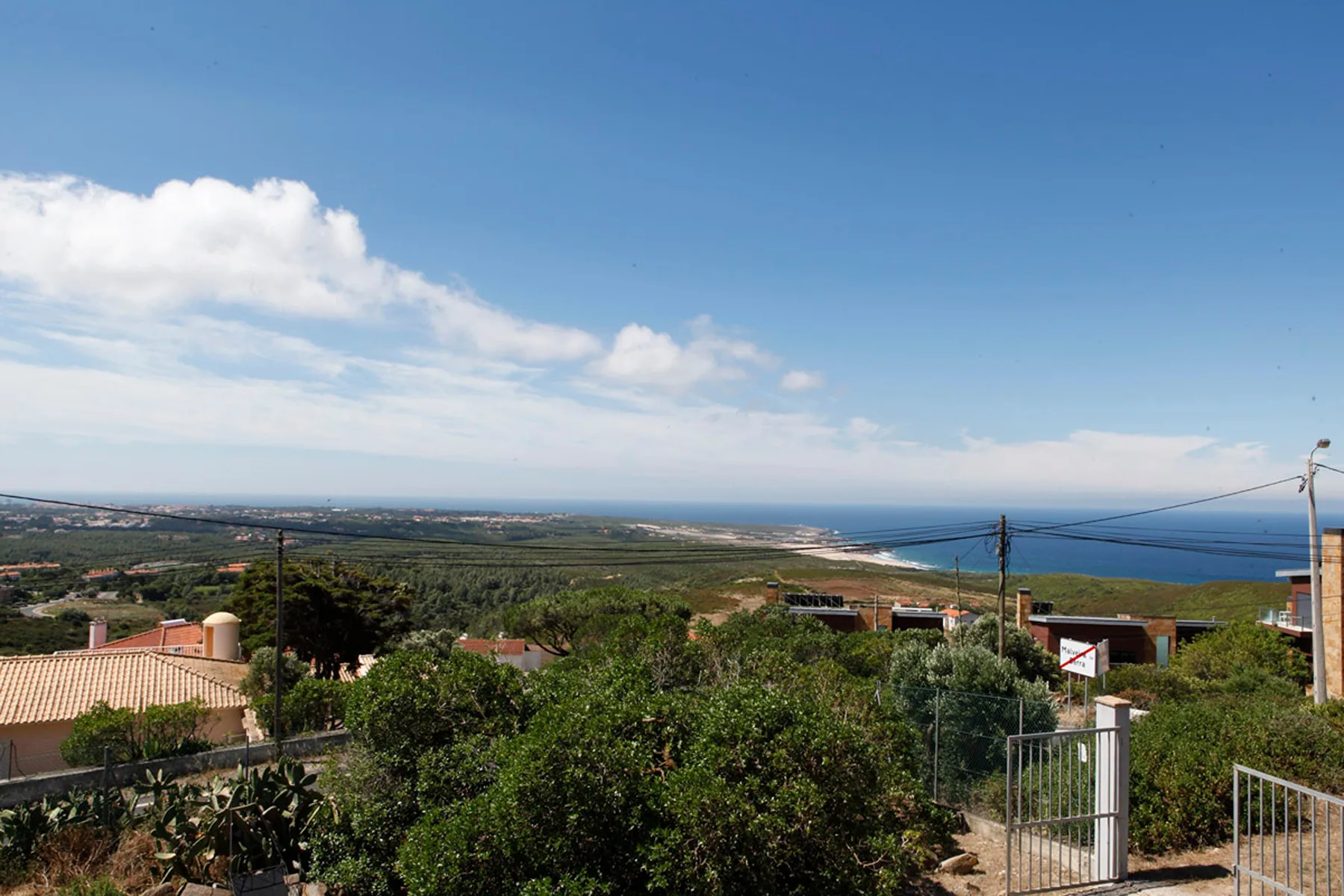 A coastal landscape with homes, greenery, and the ocean visible in the distance.