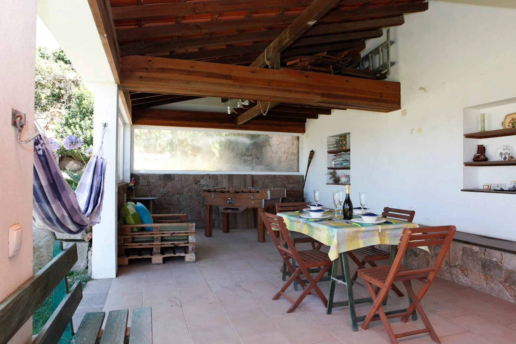 Covered patio dining area with a table and wooden seating beside a hammock.