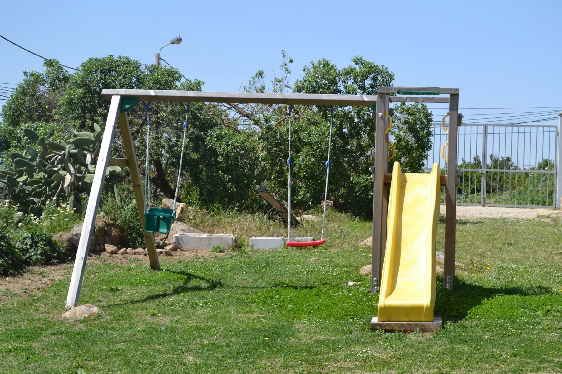 A grassy play area has a swing set and a yellow slide.