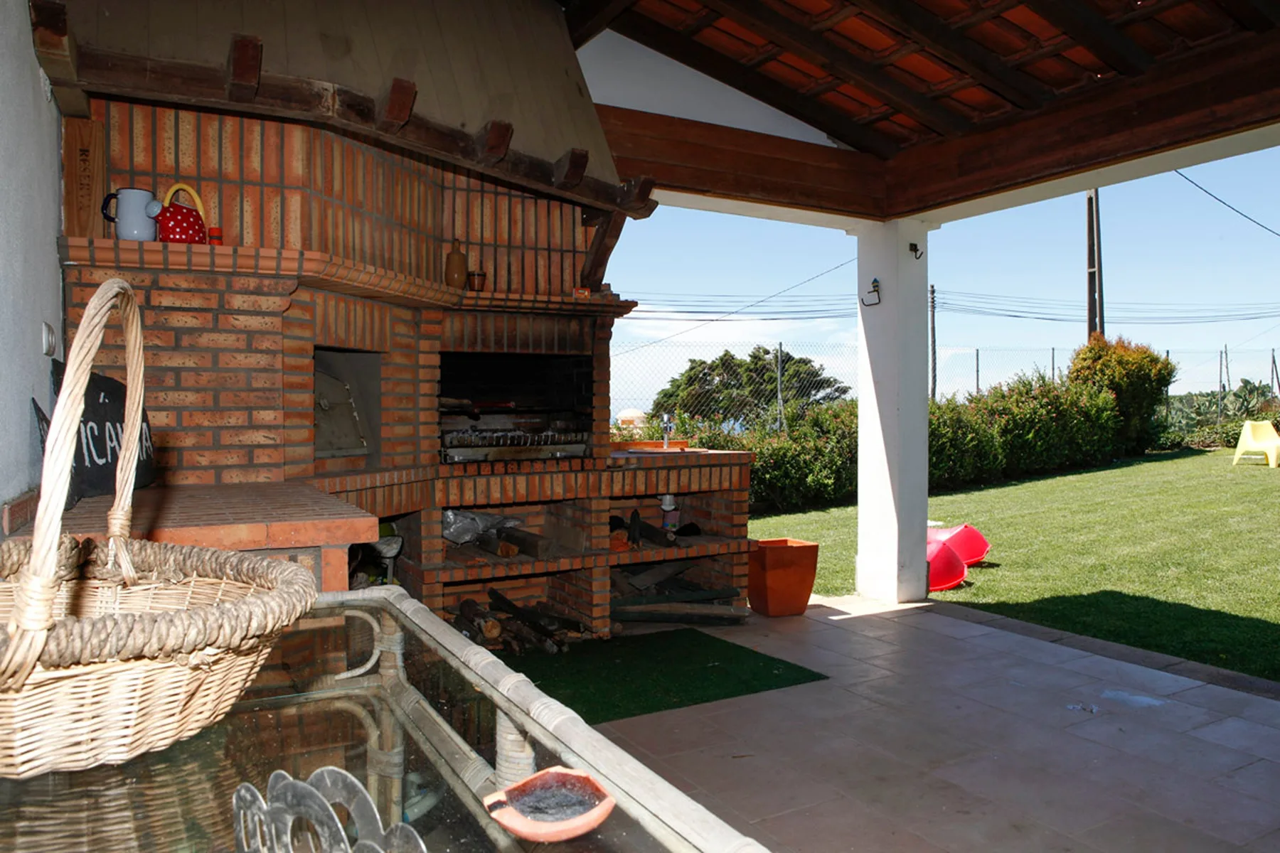 A covered outdoor patio features a brick barbecue beside a grassy garden.