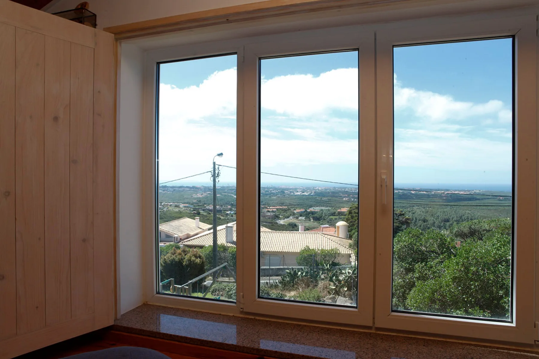 A bright room with large windows overlooking greenery and distant rooftops.