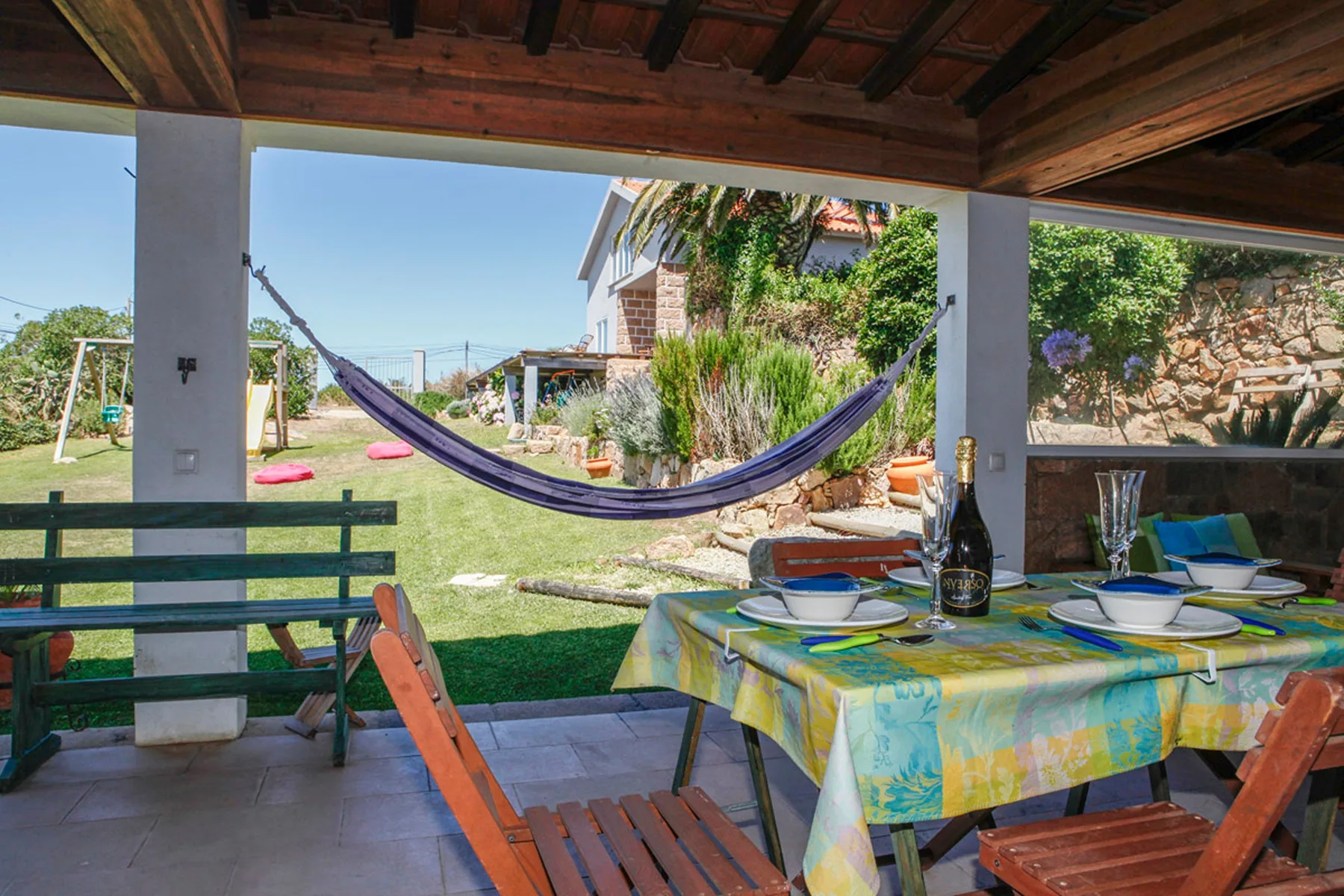 A covered patio dining area overlooks a garden with a hammock and outdoor seating.
