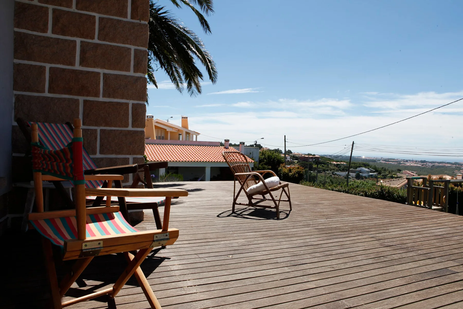 A wooden deck with colorful seating overlooks rooftops and the distant sea.