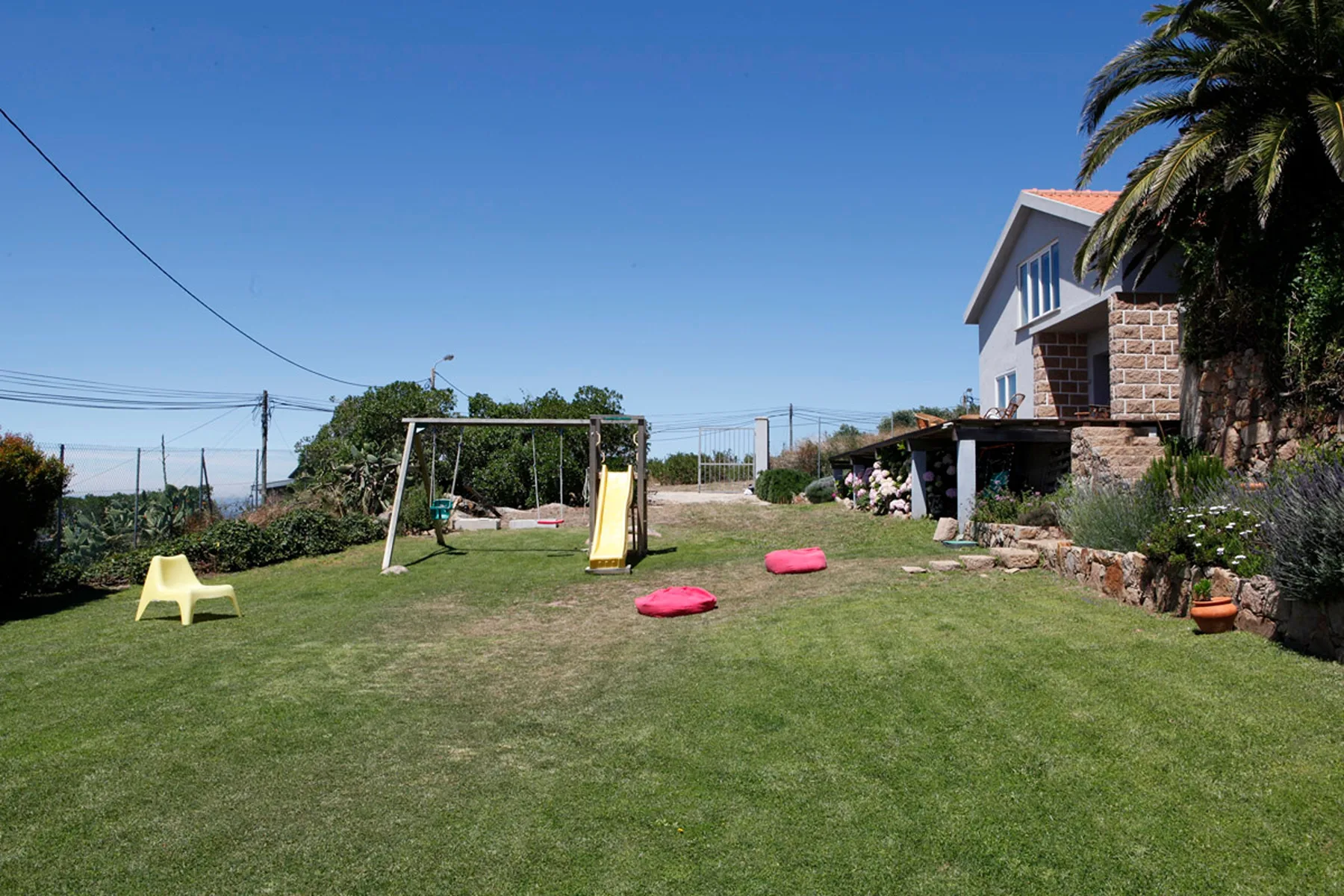 A grassy outdoor play area with a swing set and slide beside a house.