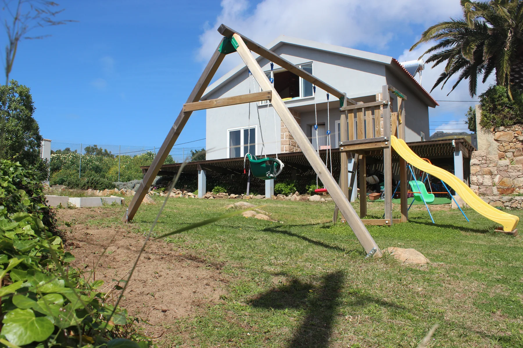 A grassy garden with a wooden play structure and a white house in the background.