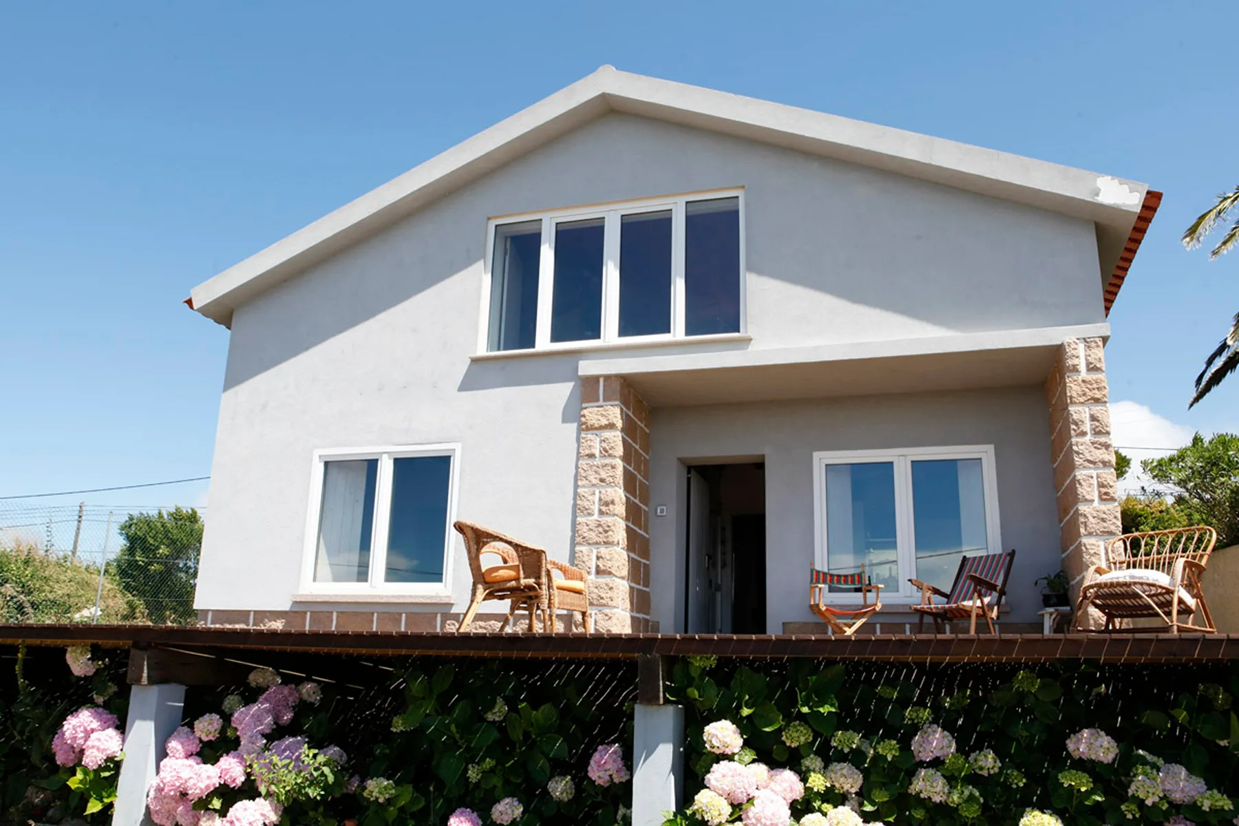 A two-story house with white walls, stone accents, and a flower garden.