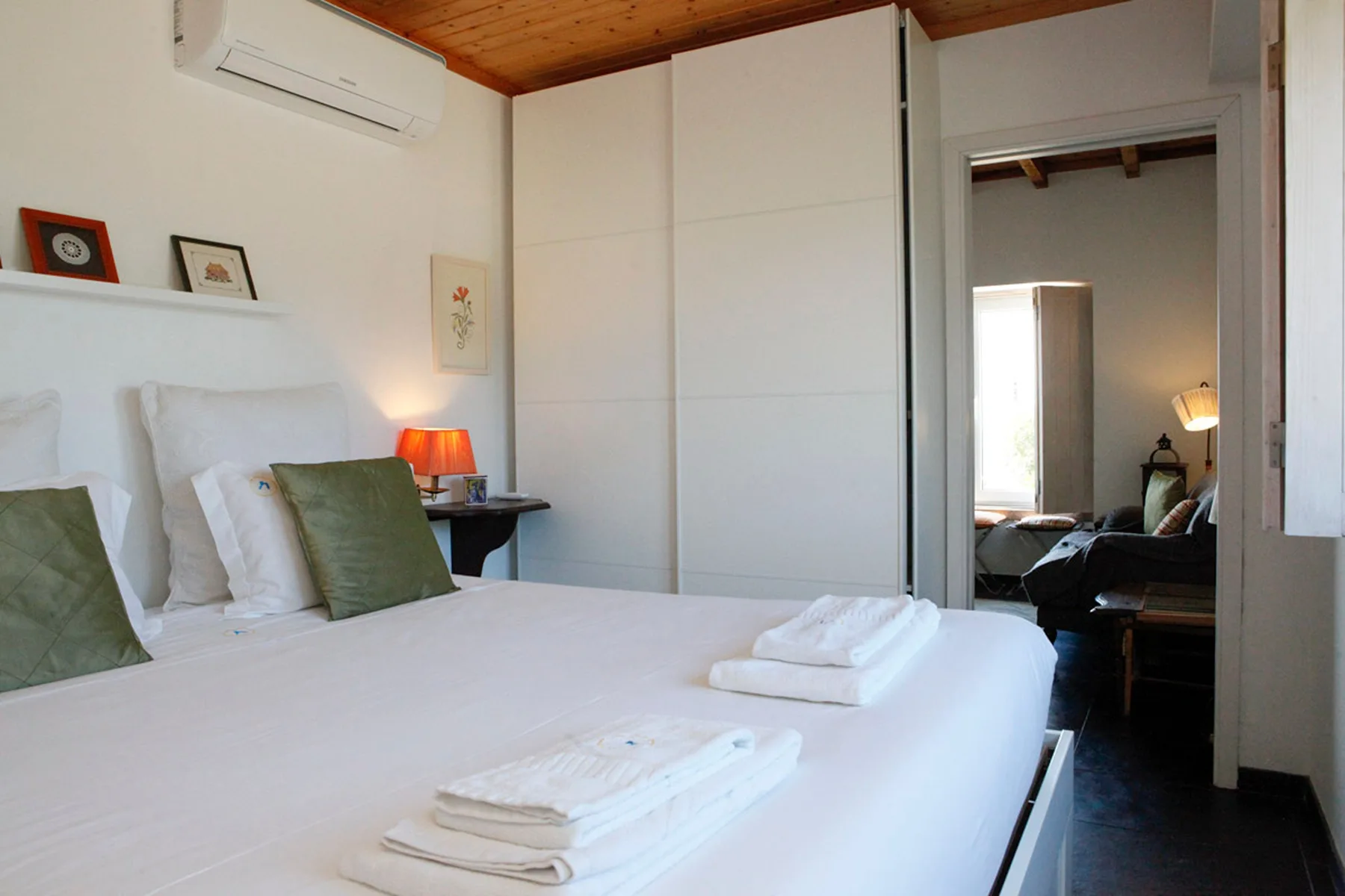 A bedroom with a neatly made bed and an open doorway to a sitting area.