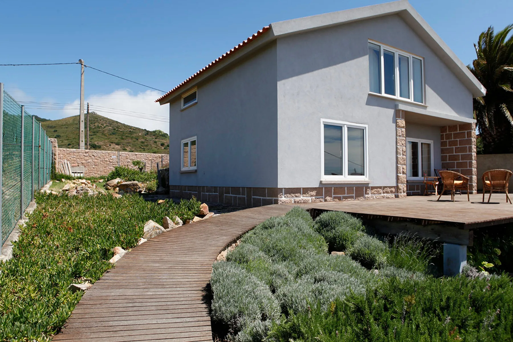 A modern house stands beside a wooden walkway through a landscaped garden.