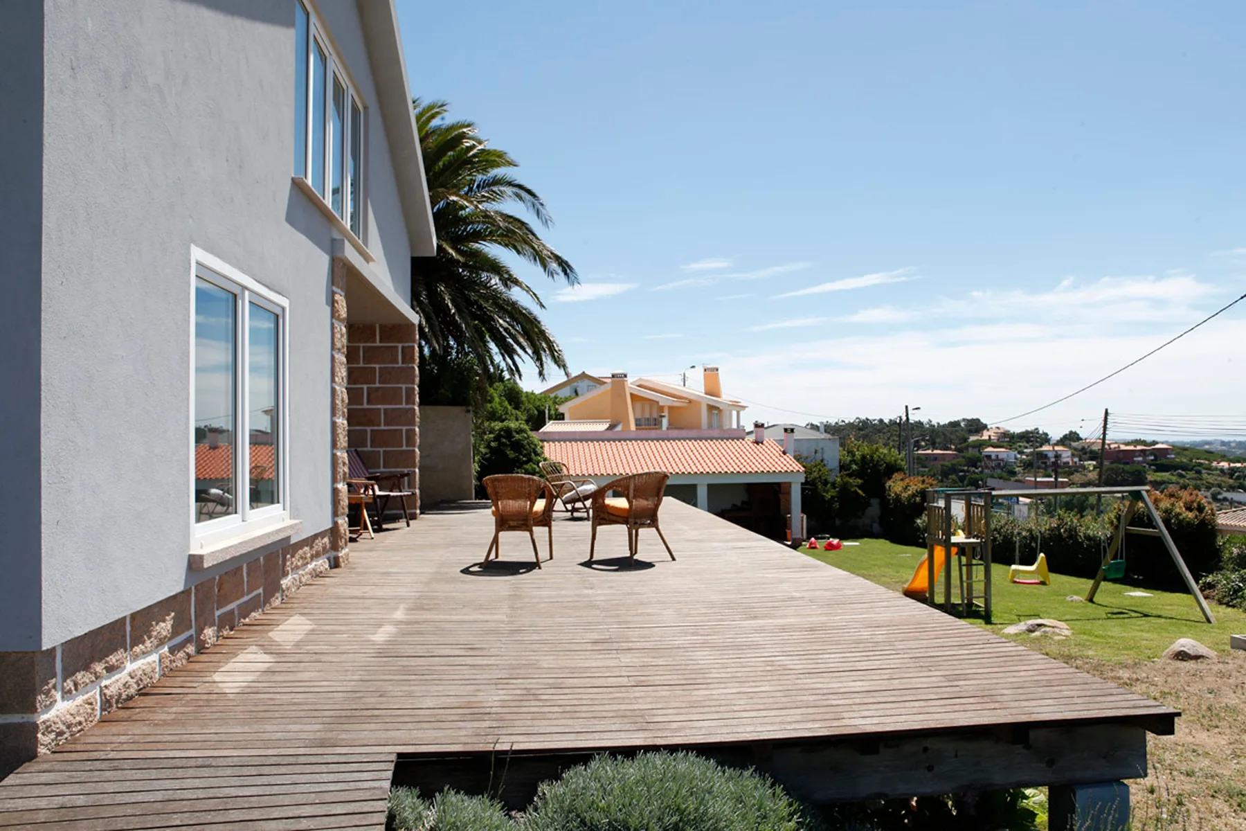 A house patio with outdoor seating overlooks a garden and nearby homes.