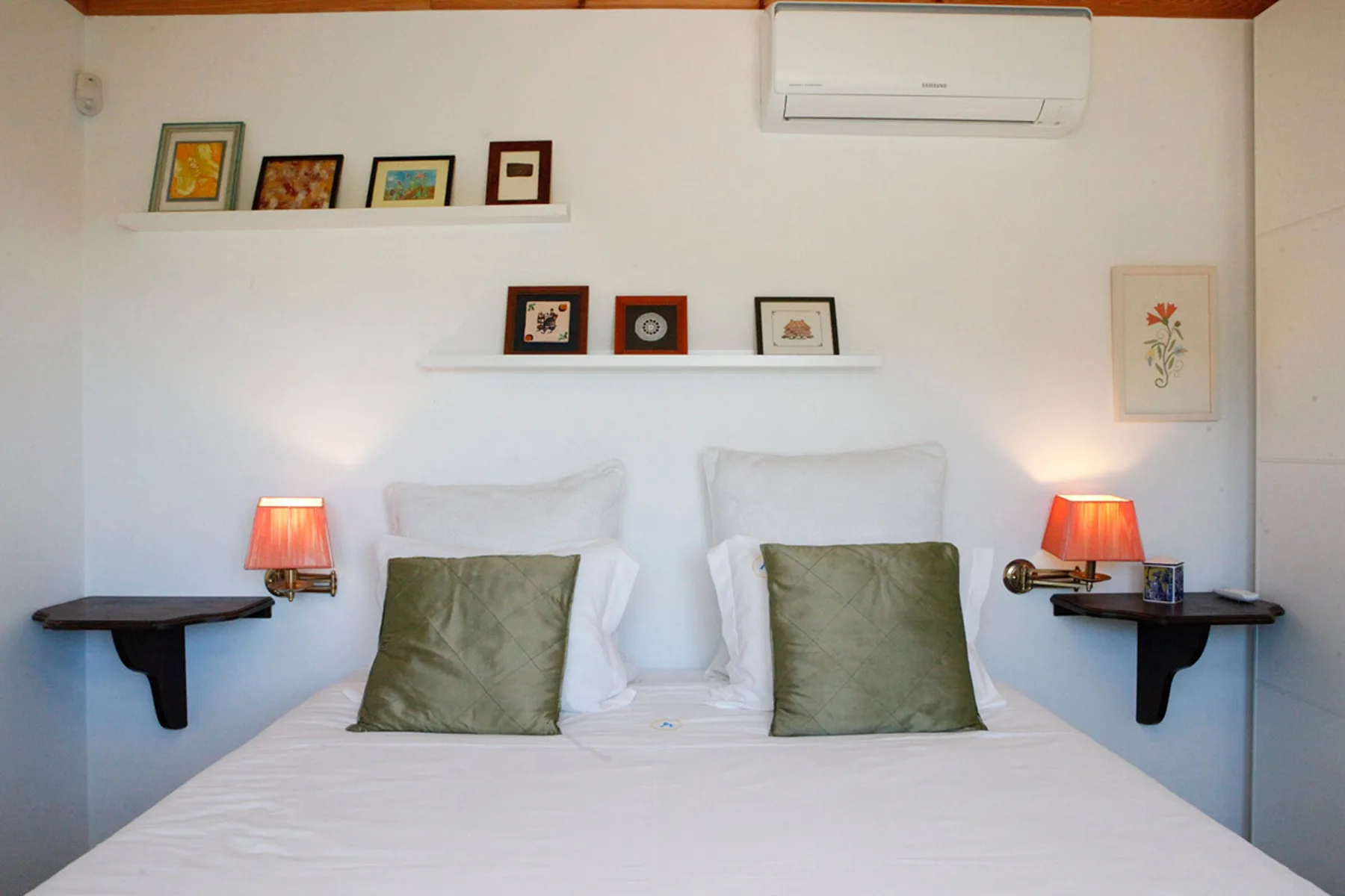 A bedroom with a bed, green pillows, and framed artwork on the walls.