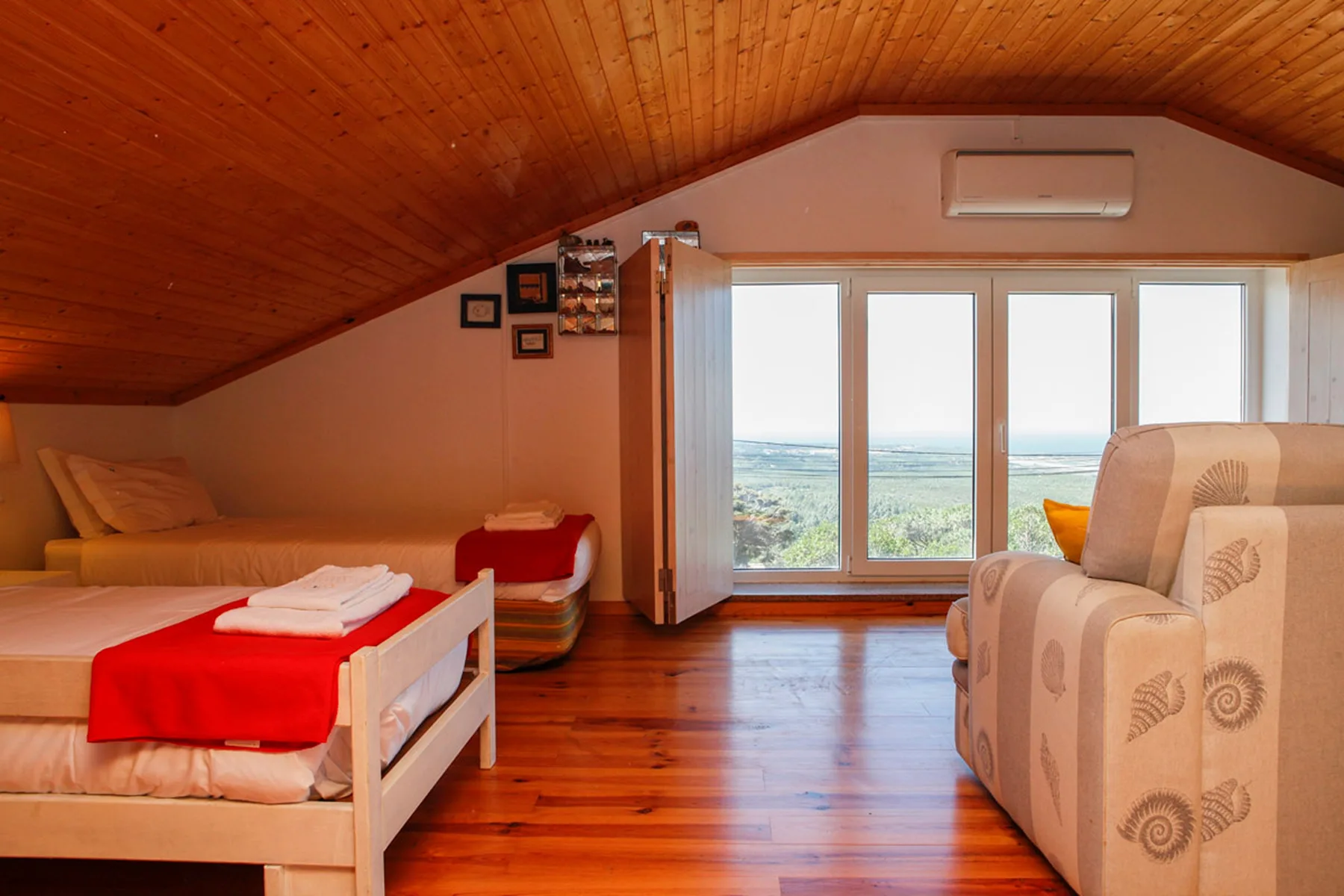 A bright bedroom with a bed beside wide windows overlooking the sea.