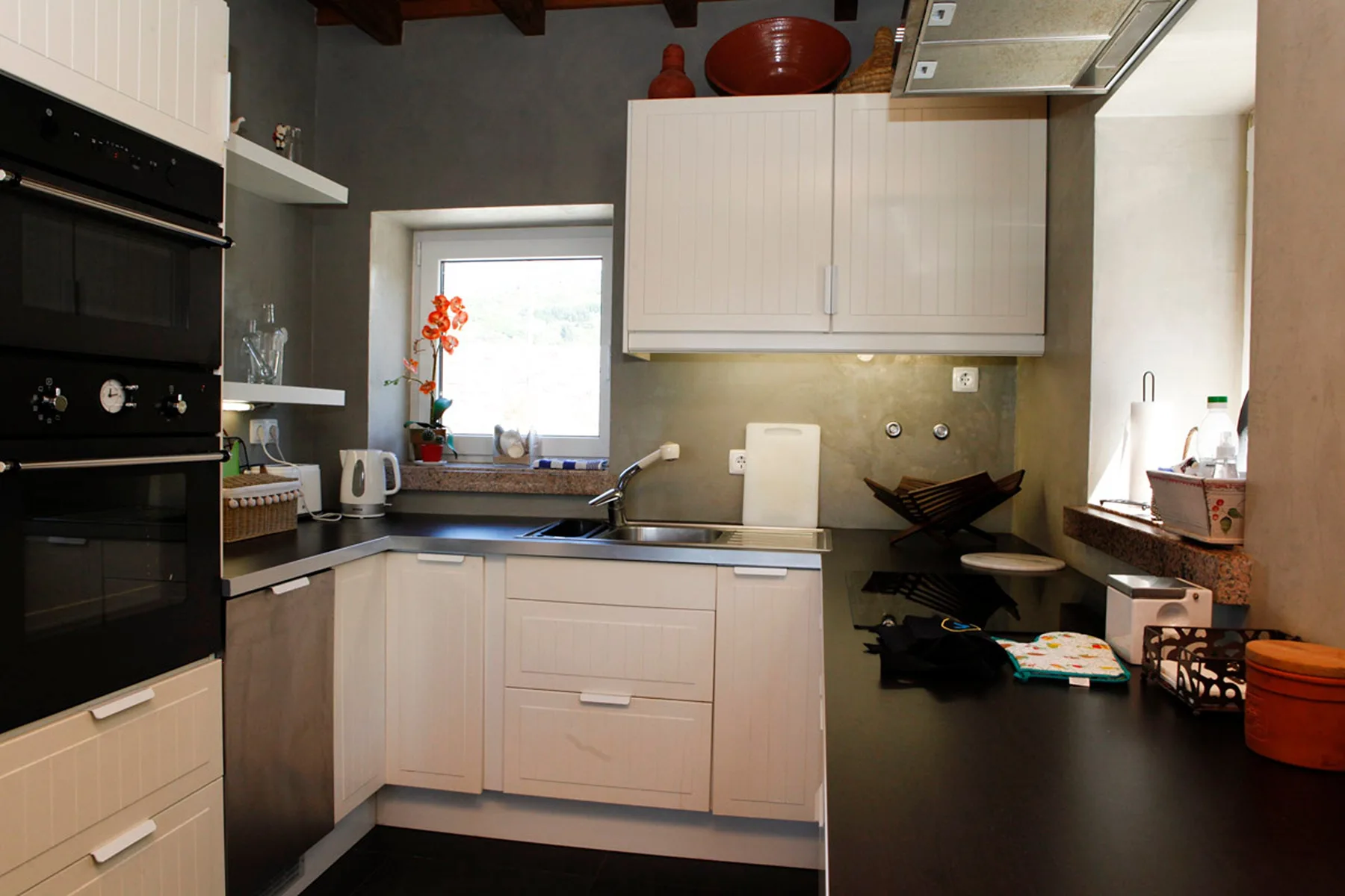 A kitchen with pale cabinets, dark countertops, and a window above the sink.