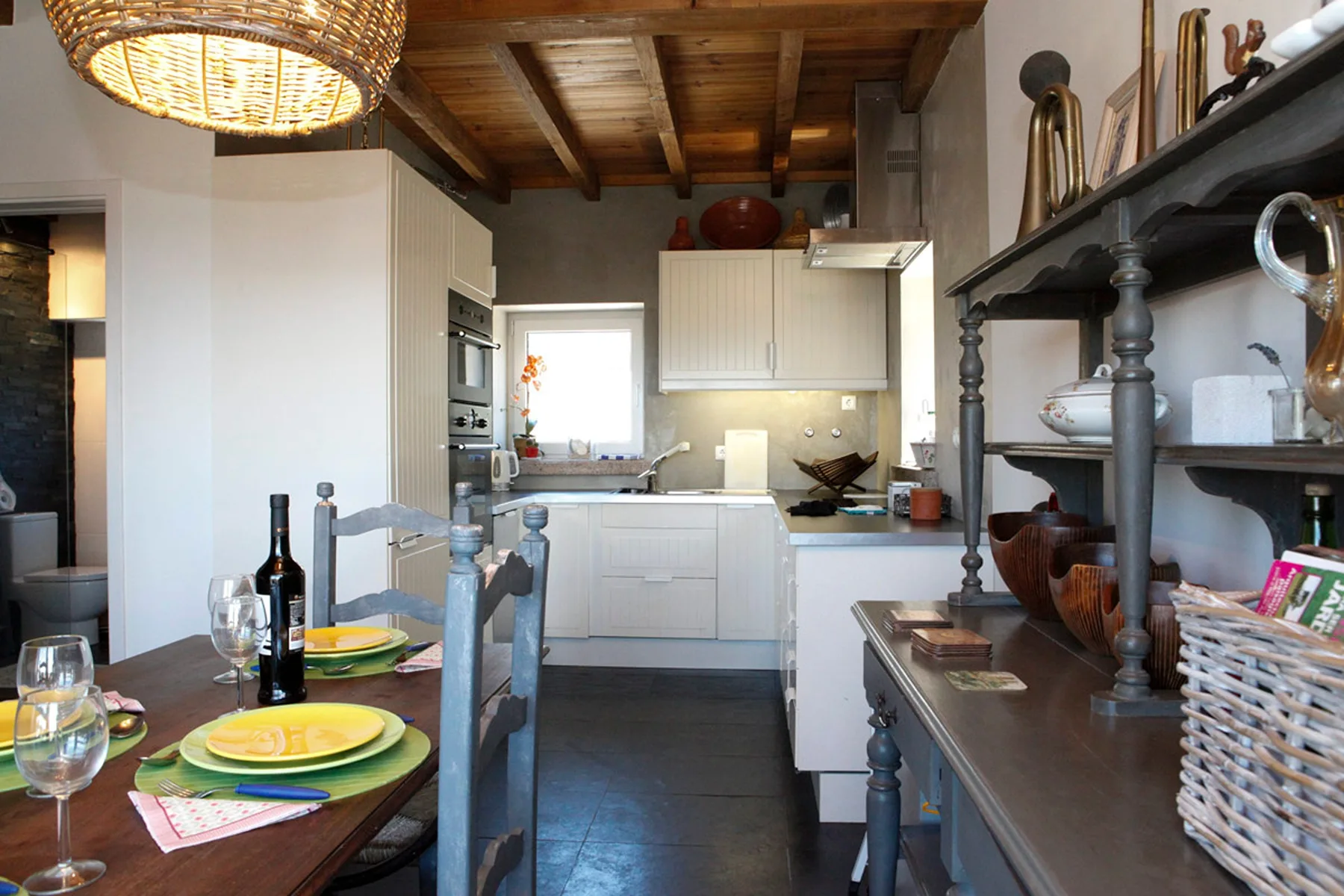 A kitchen with white cabinetry, wooden ceiling beams, and a dining table.