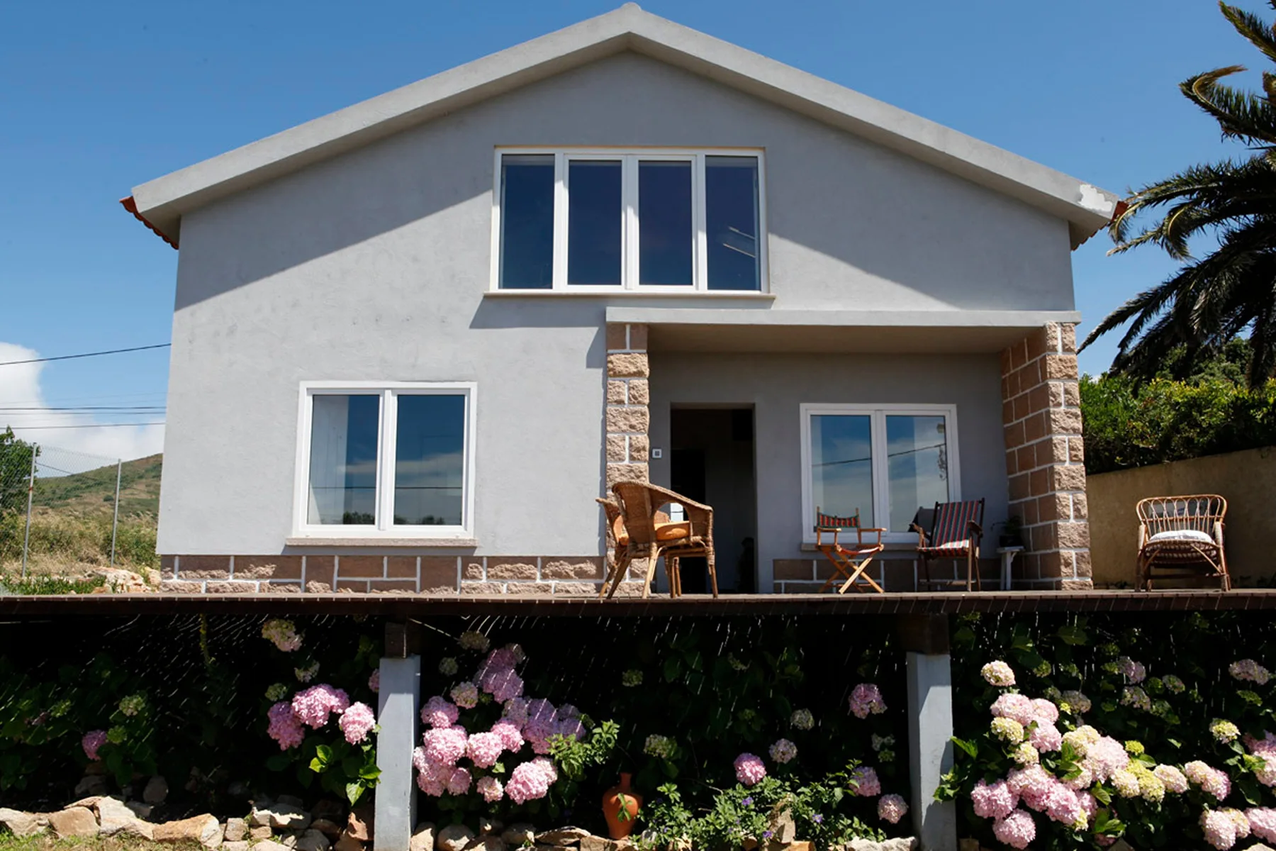 A gray two-story house with a covered patio and flowering garden.