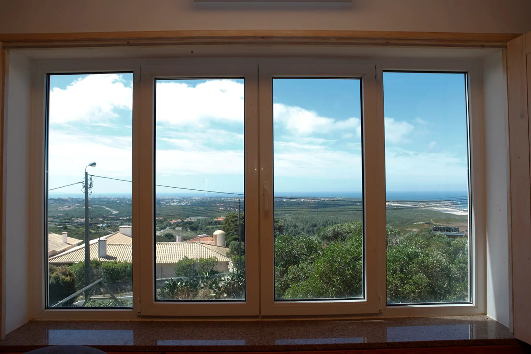 A large window overlooks green hills and the sea beneath a partly cloudy sky.