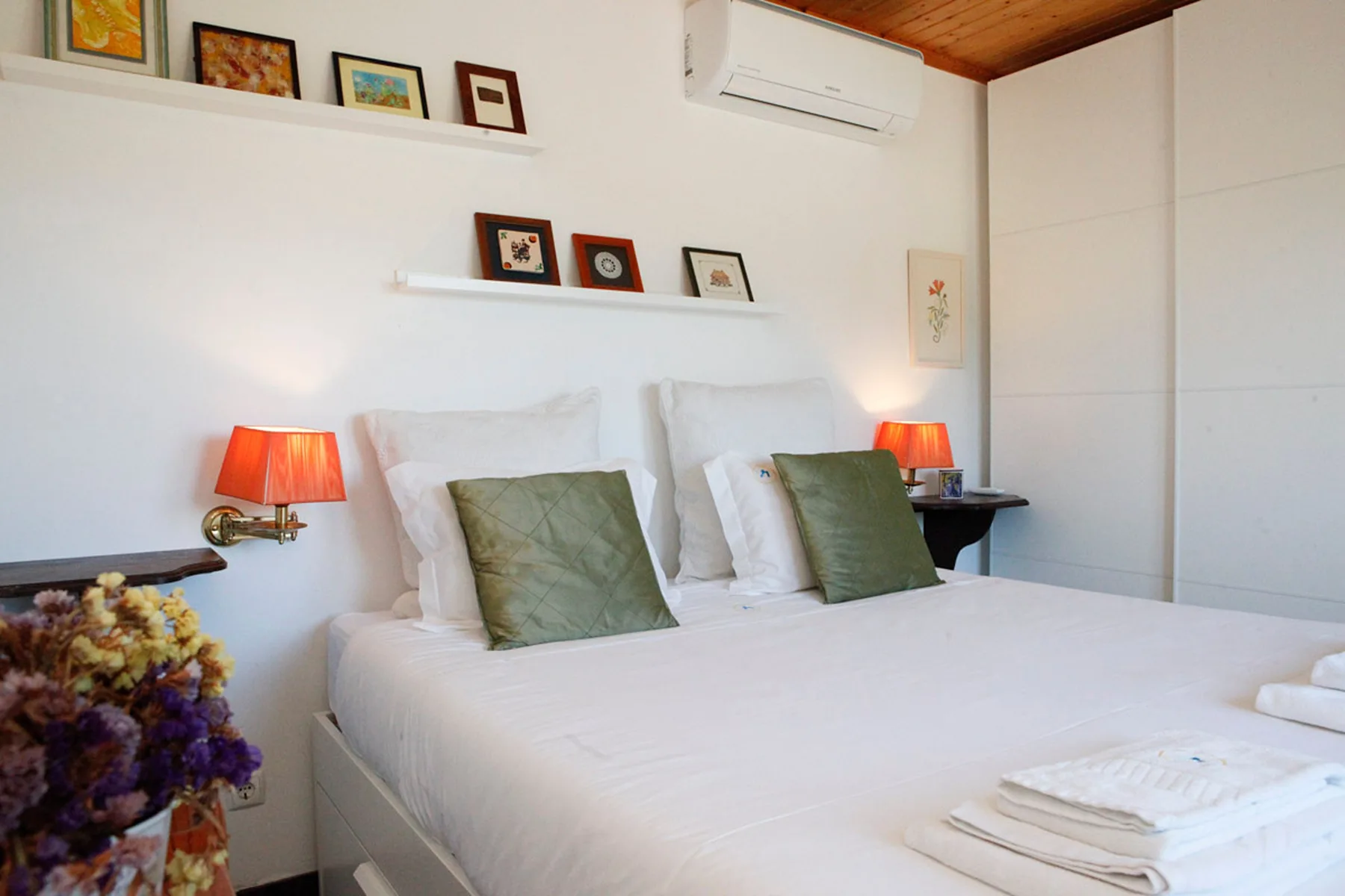 A bedroom with a neatly made bed, green cushions, and bedside lamps.
