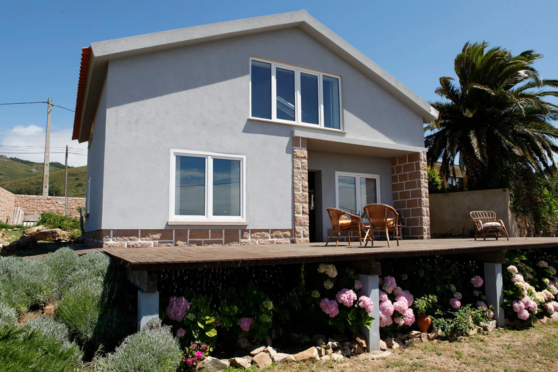 A modern house with a raised wooden deck, outdoor seating, and flowering plants.