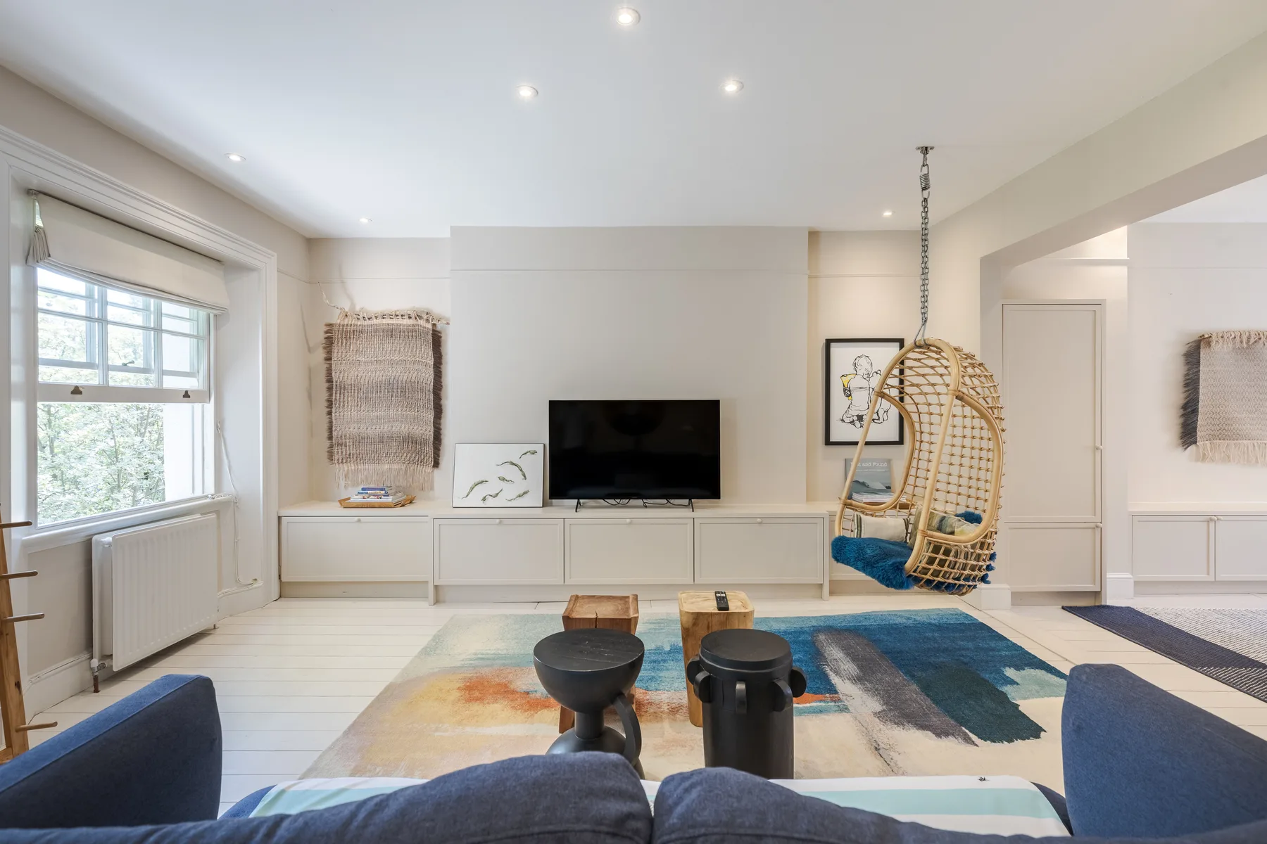 A bright living room with a television, seating, and a hanging chair.