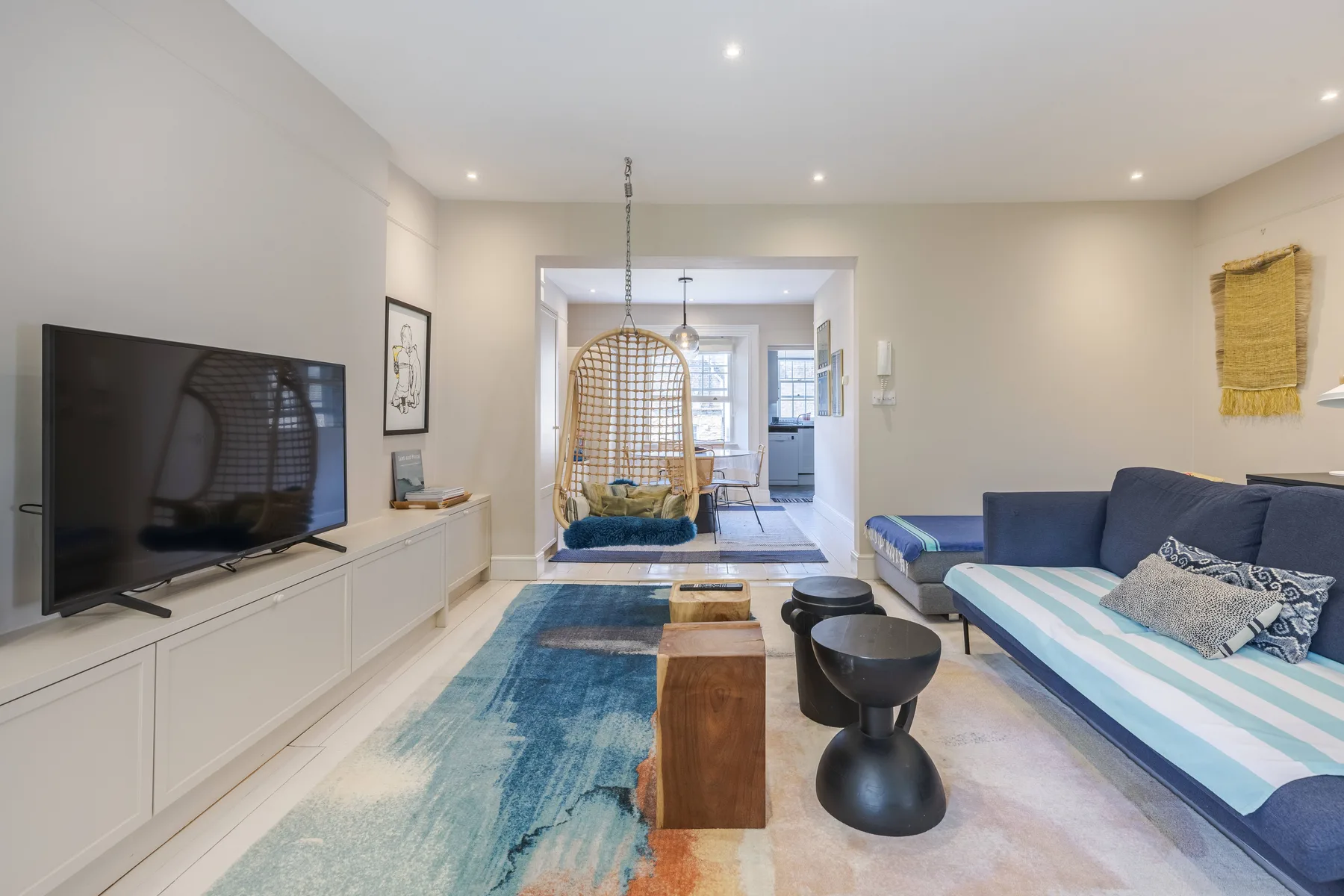 A bright living room with a television, seating, and a hanging chair.