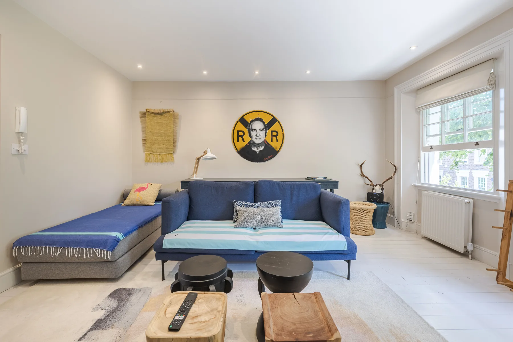 A bright living room with blue seating, a large window, and a round wall decoration.