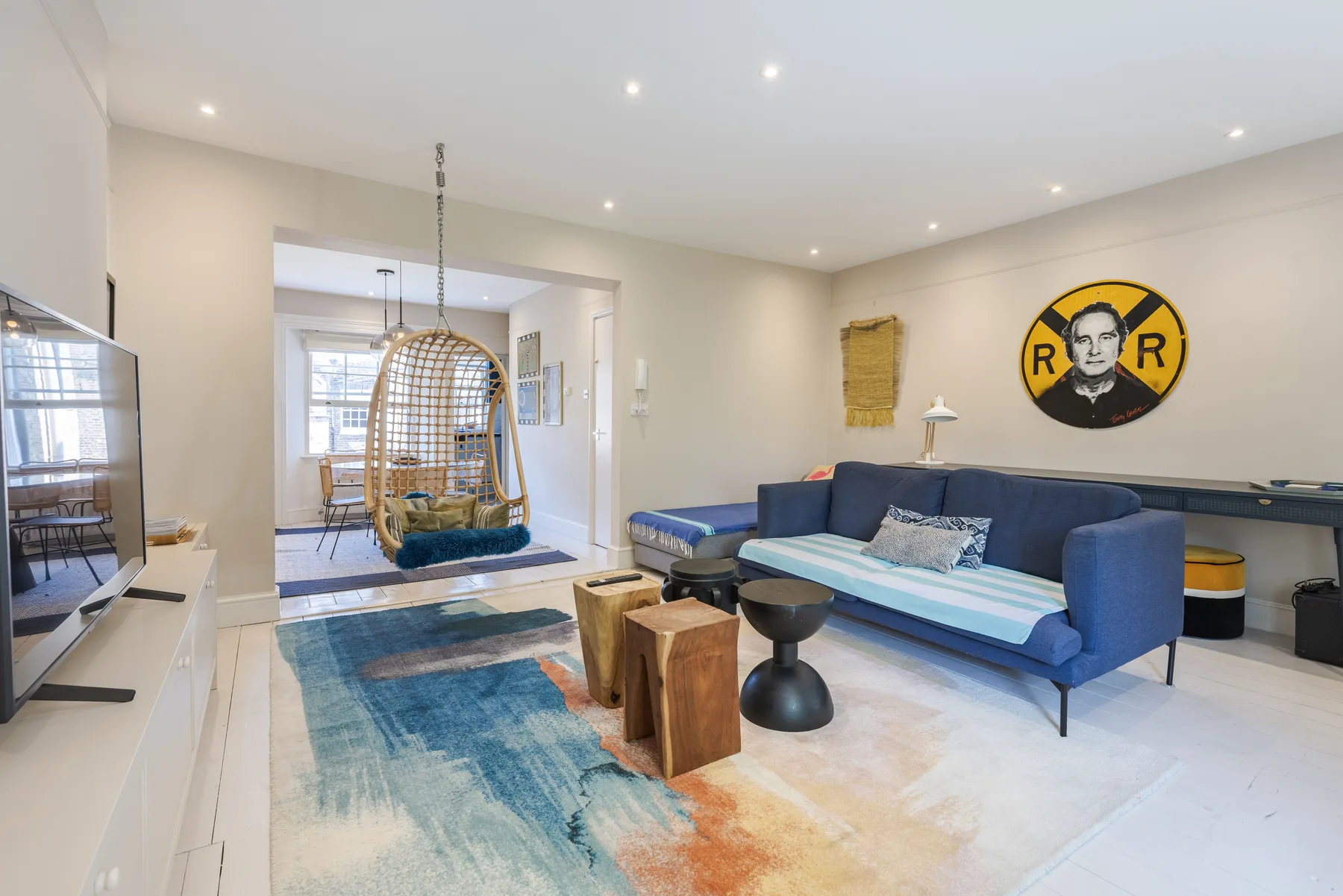 A bright living room with blue seating, a rug, and a hanging chair.