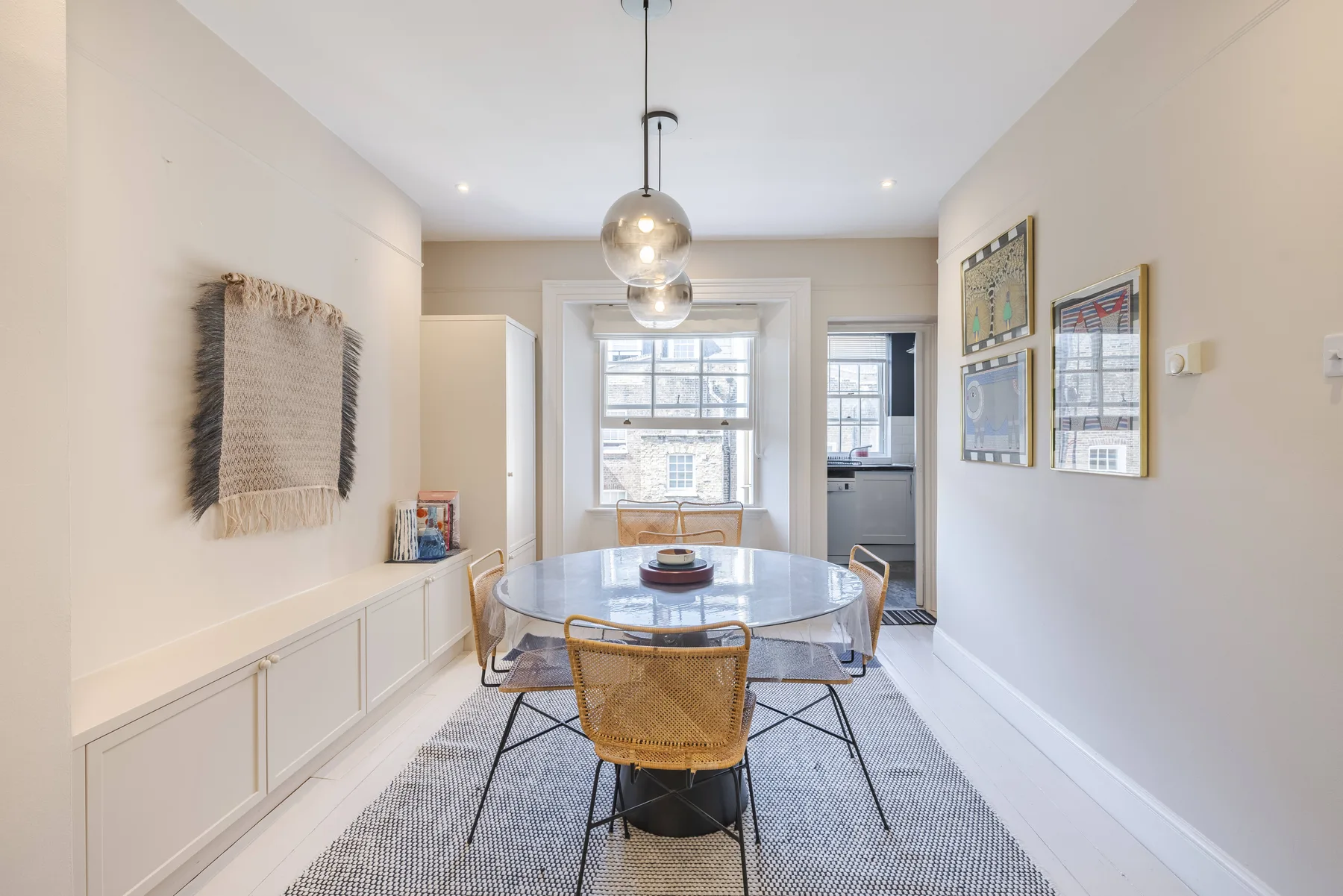 A bright dining room with a round glass table and woven seating.