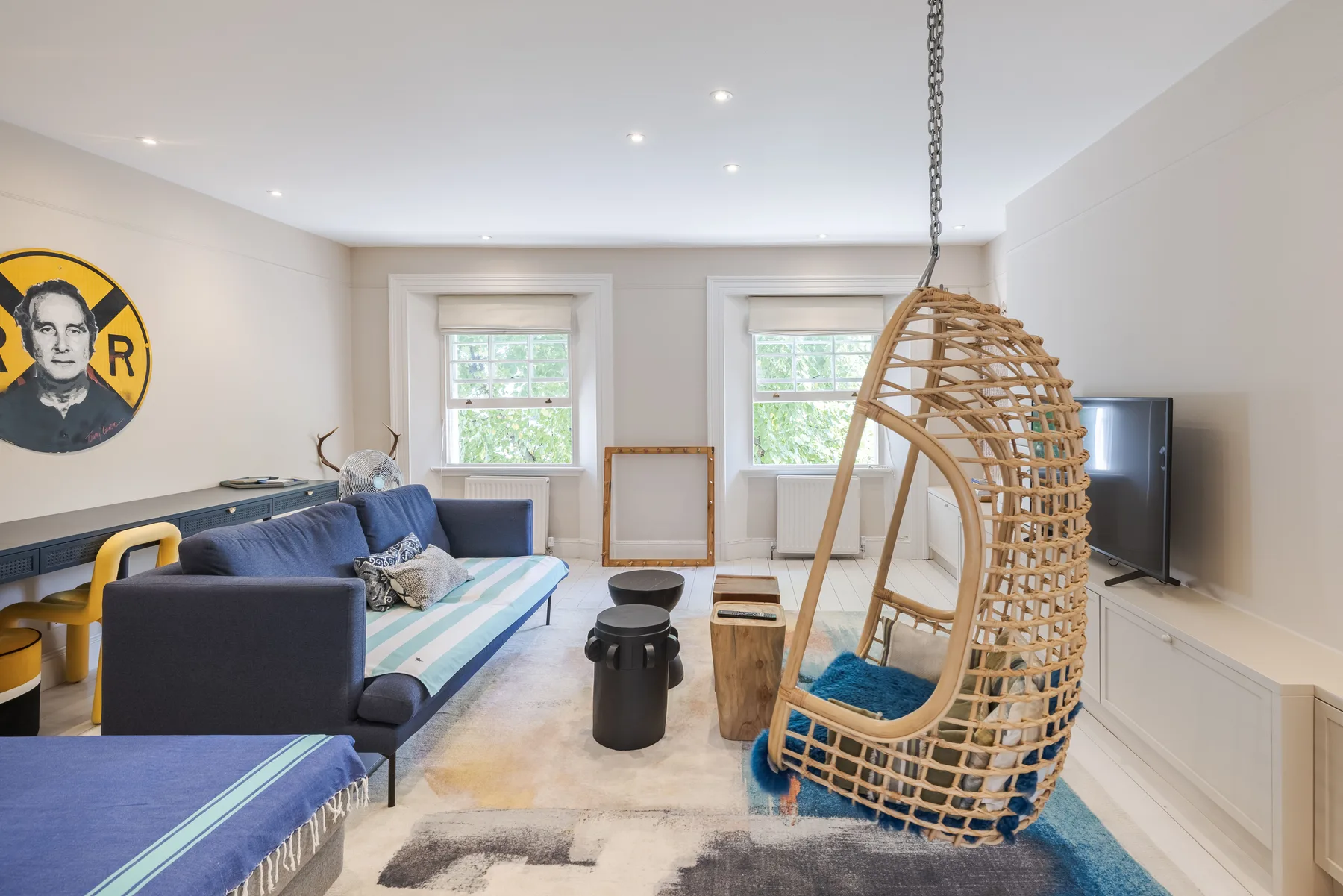A bright living room with blue seating and a hanging wicker chair.