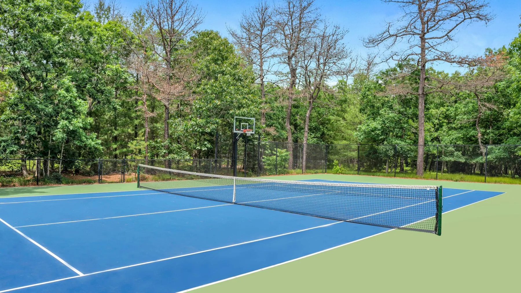Una cancha de tenis al aire libre con una canasta de baloncesto detrás de la red.