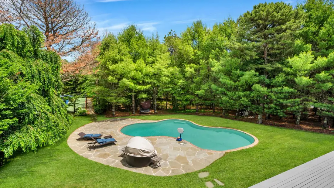 Una piscina en el patio está rodeada por un patio de piedra y césped verde.