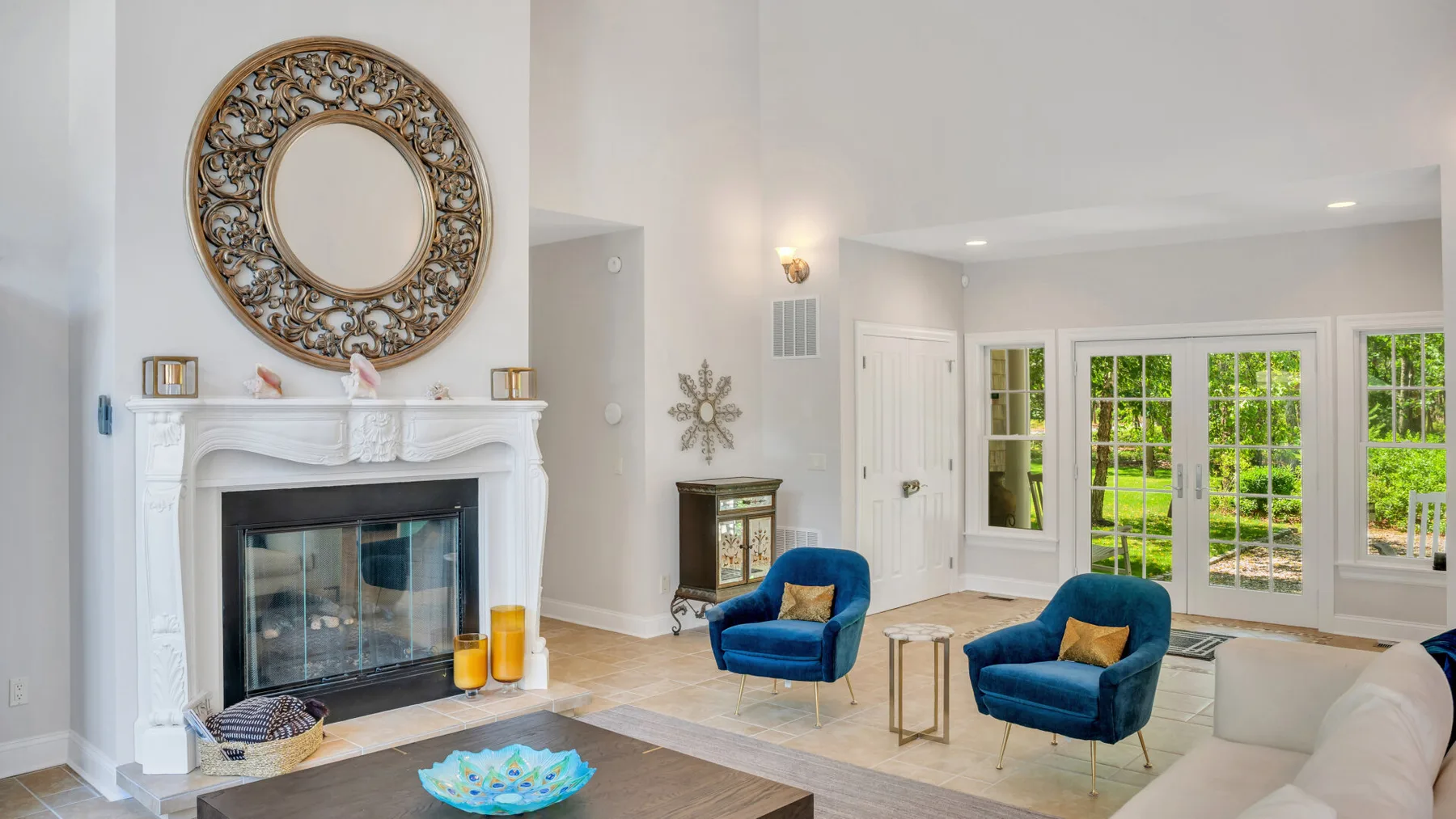 Una sala luminosa con chimenea, asientos azules y ventanas con vista al jardín.