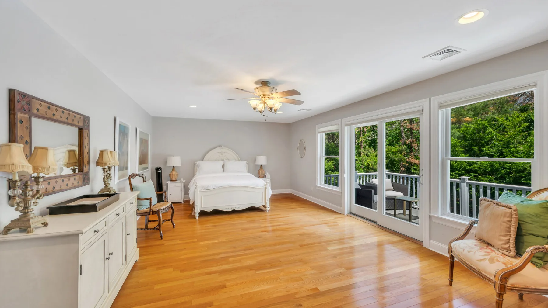 Un dormitorio luminoso con una cama, suelo de madera y ventanas amplias.