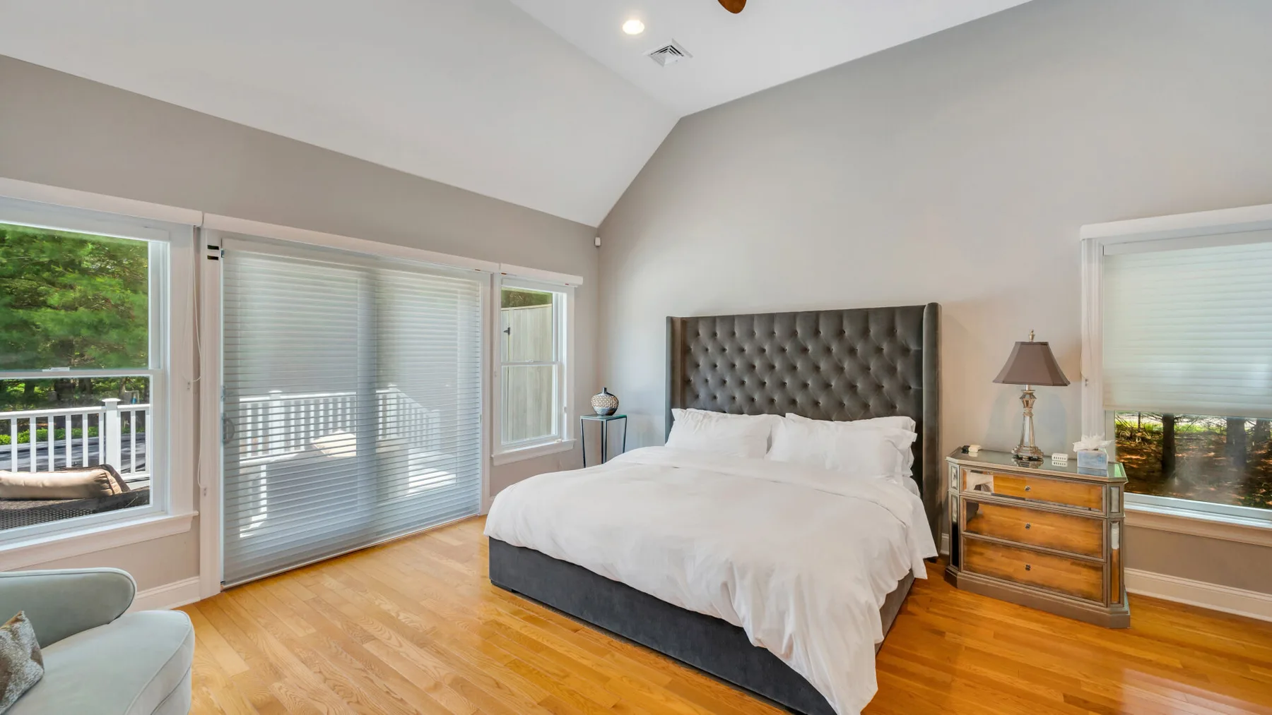 Un dormitorio luminoso con una cama grande, suelo de madera y ventanas amplias.
