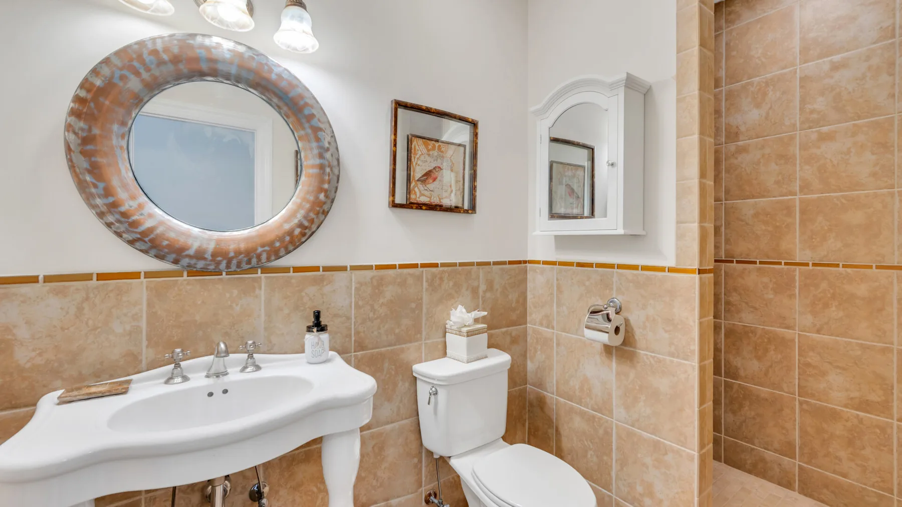 Un baño con azulejos, lavabo, inodoro y espejo redondo.