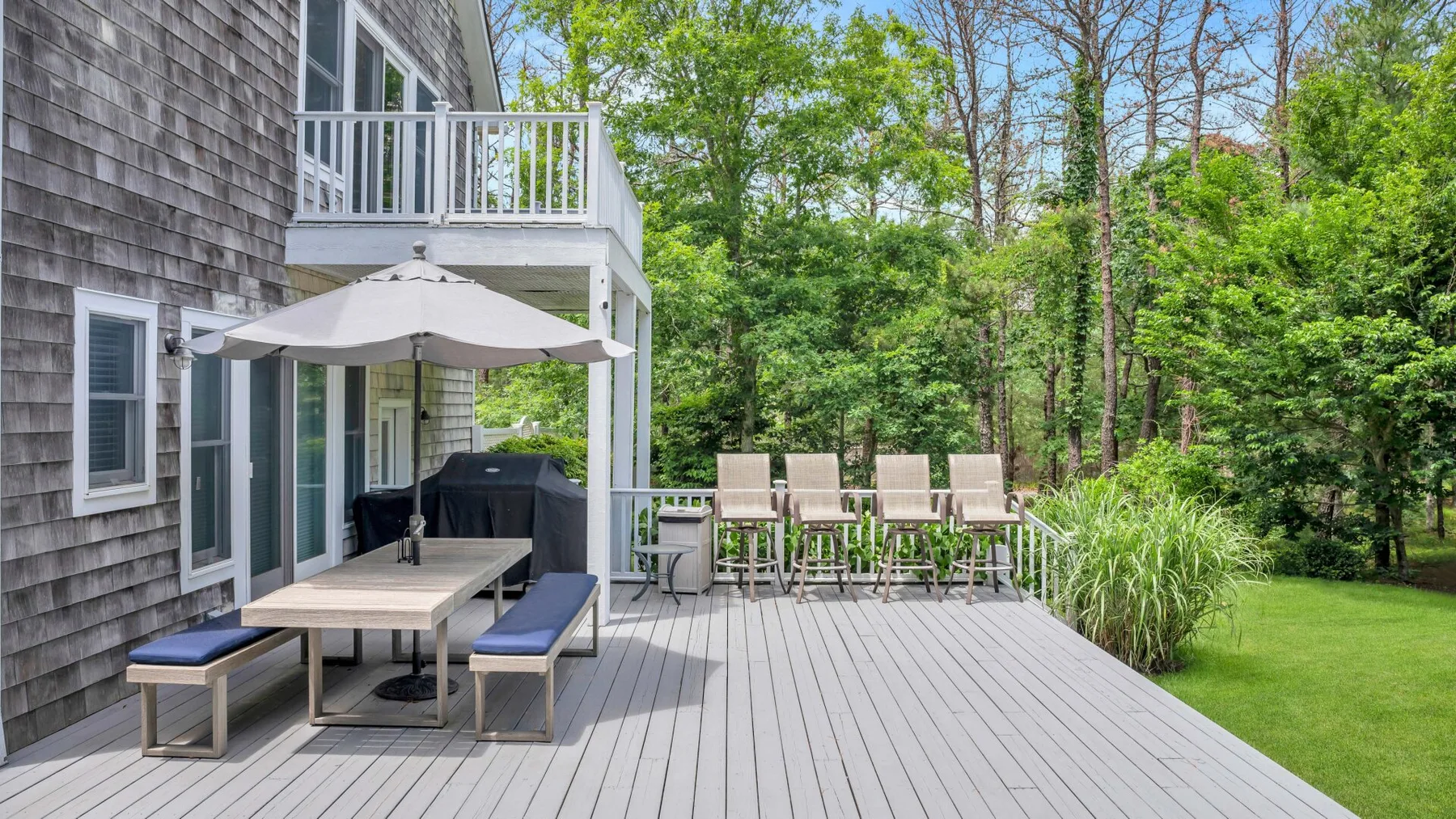Una terraza exterior con una mesa de comedor y asientos junto a un jardín arbolado.