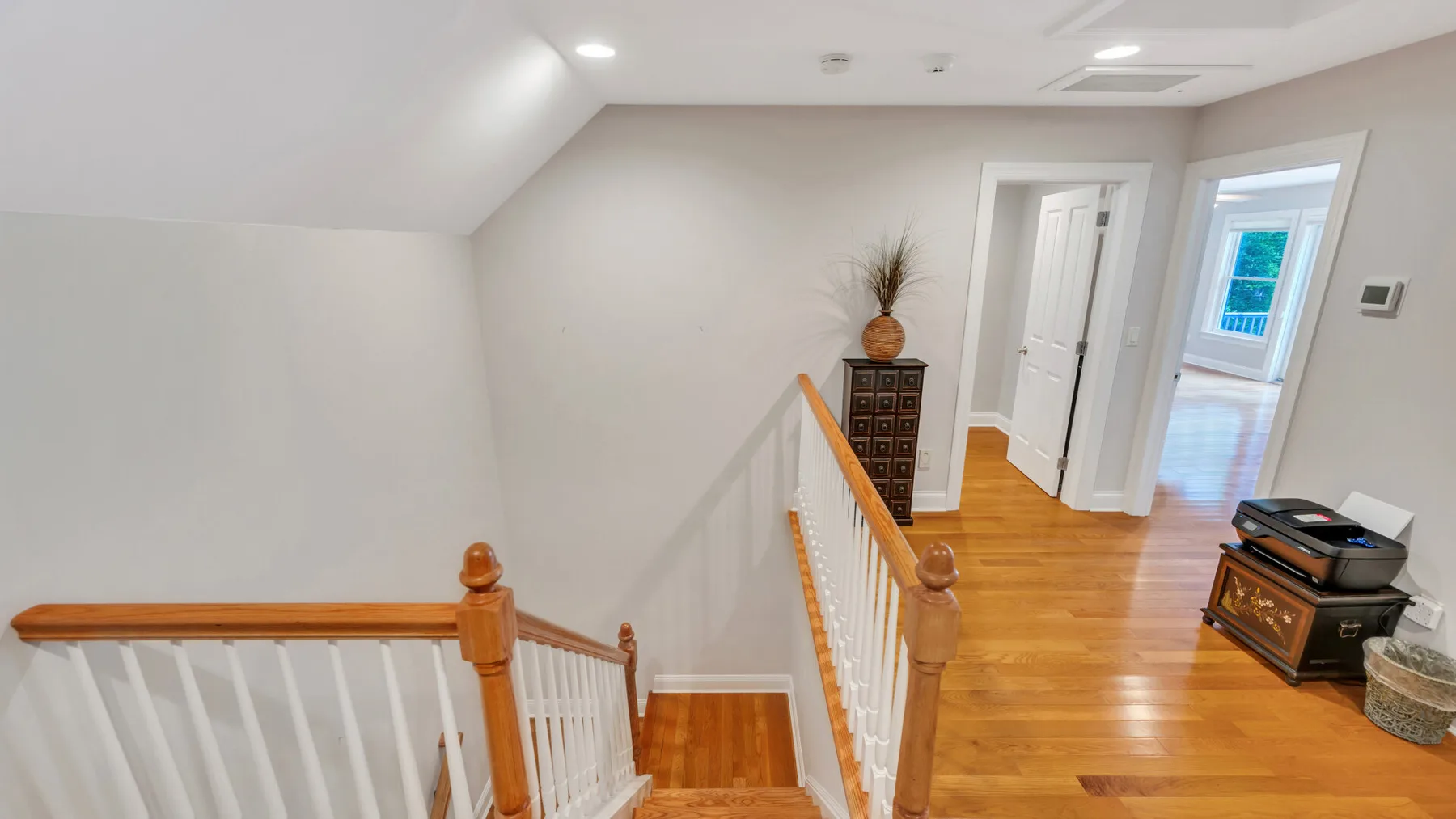 Un rellano luminoso en la planta superior con suelo de madera y una escalera.
