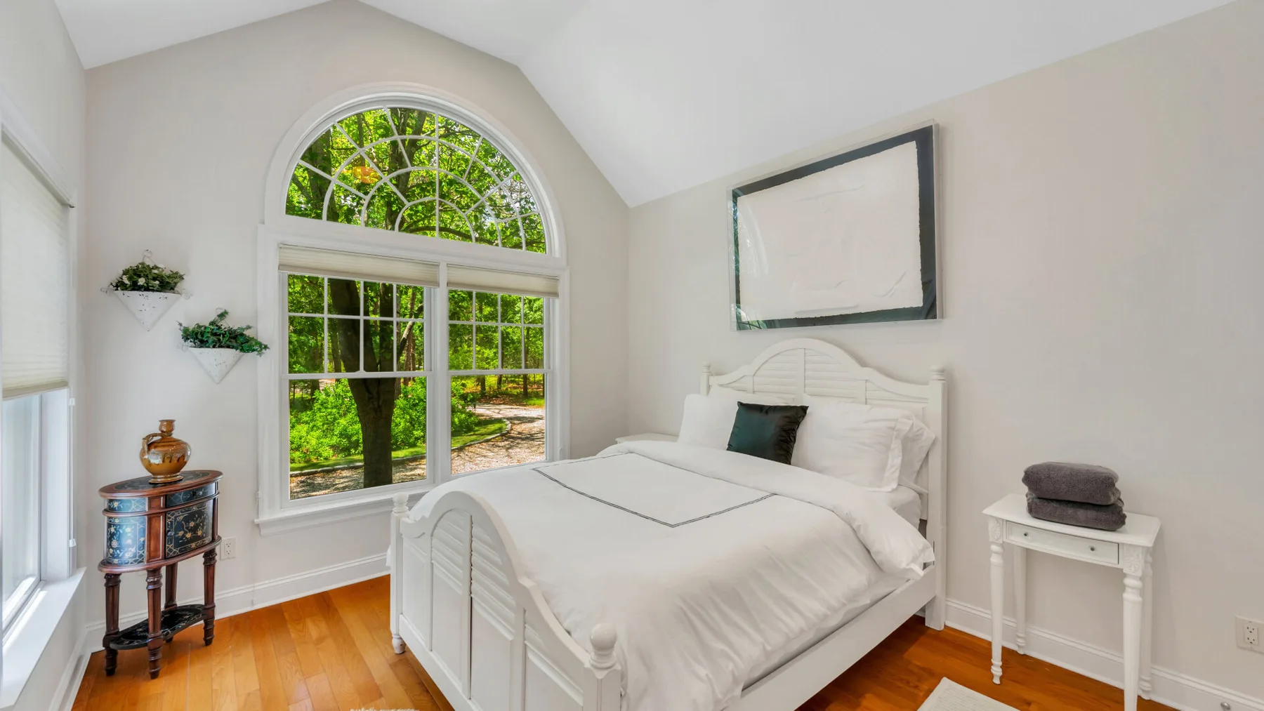 Un dormitorio luminoso con una cama blanca junto a una gran ventana arqueada.