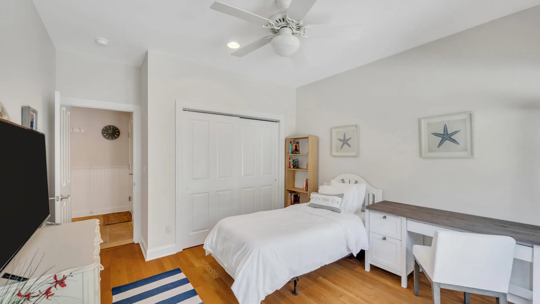 Un dormitorio luminoso con cama, escritorio y ventilador de techo.