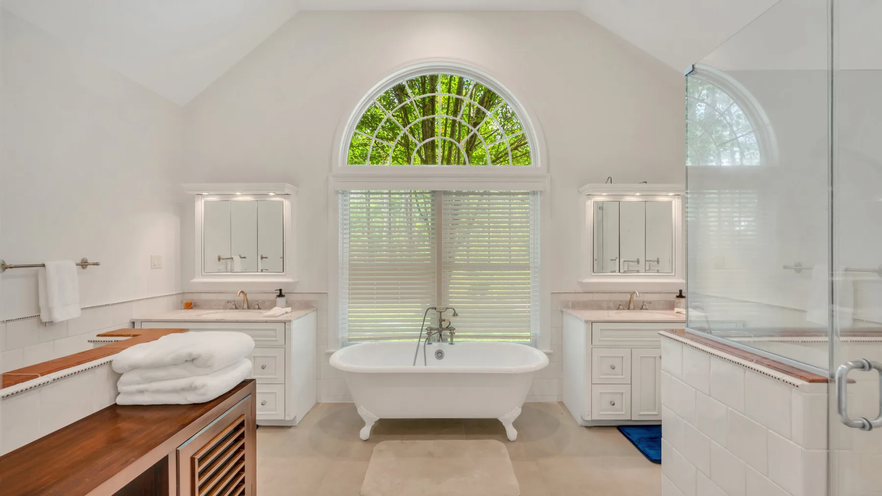 Un baño luminoso tiene una bañera exenta bajo una ventana arqueada.