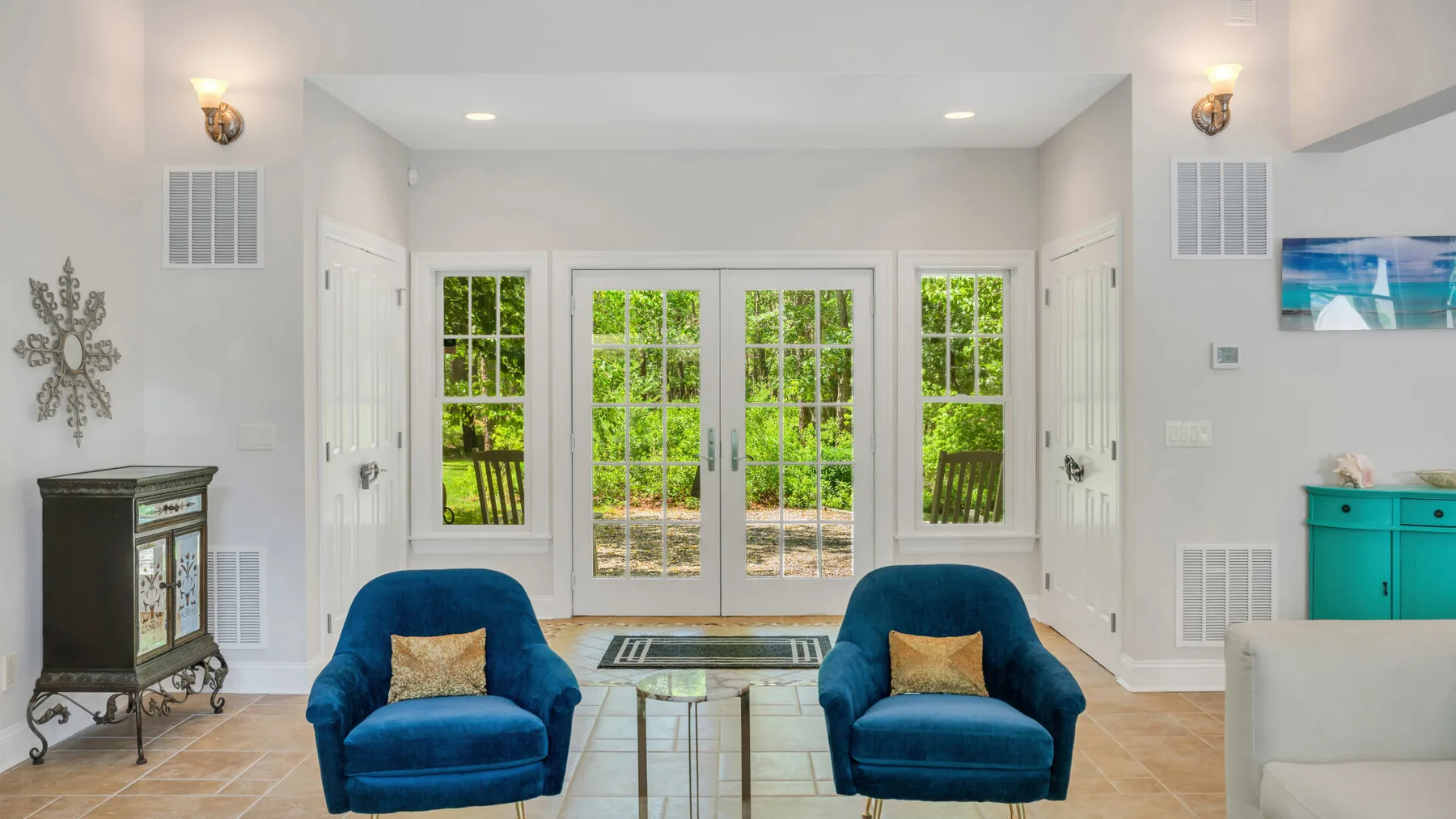 Una sala luminosa con dos sillones azules frente a puertas y ventanas de vidrio.