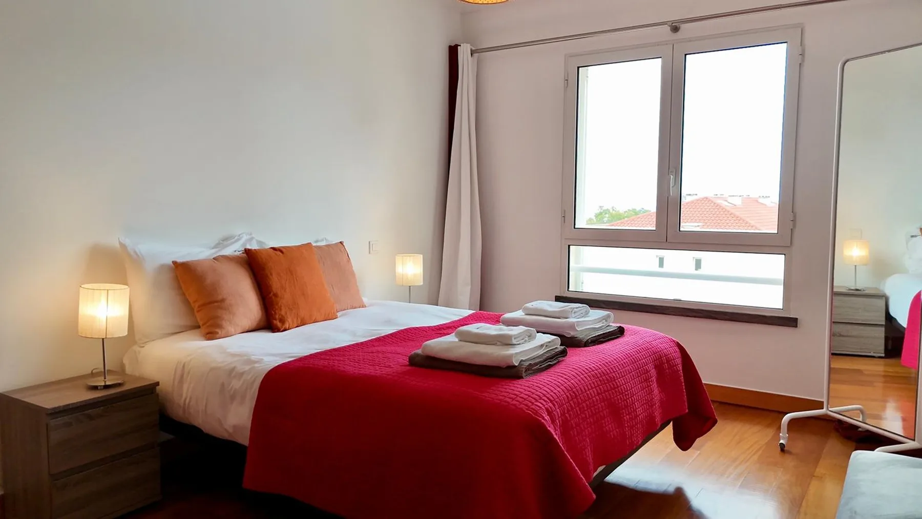 Un dormitorio con una cama cubierta por una manta roja junto a una ventana grande.