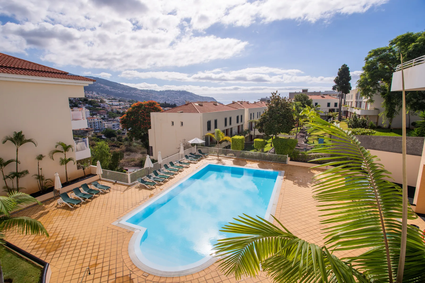 Outdoor swimming pool surrounded by lounge chairs and apartment buildings.