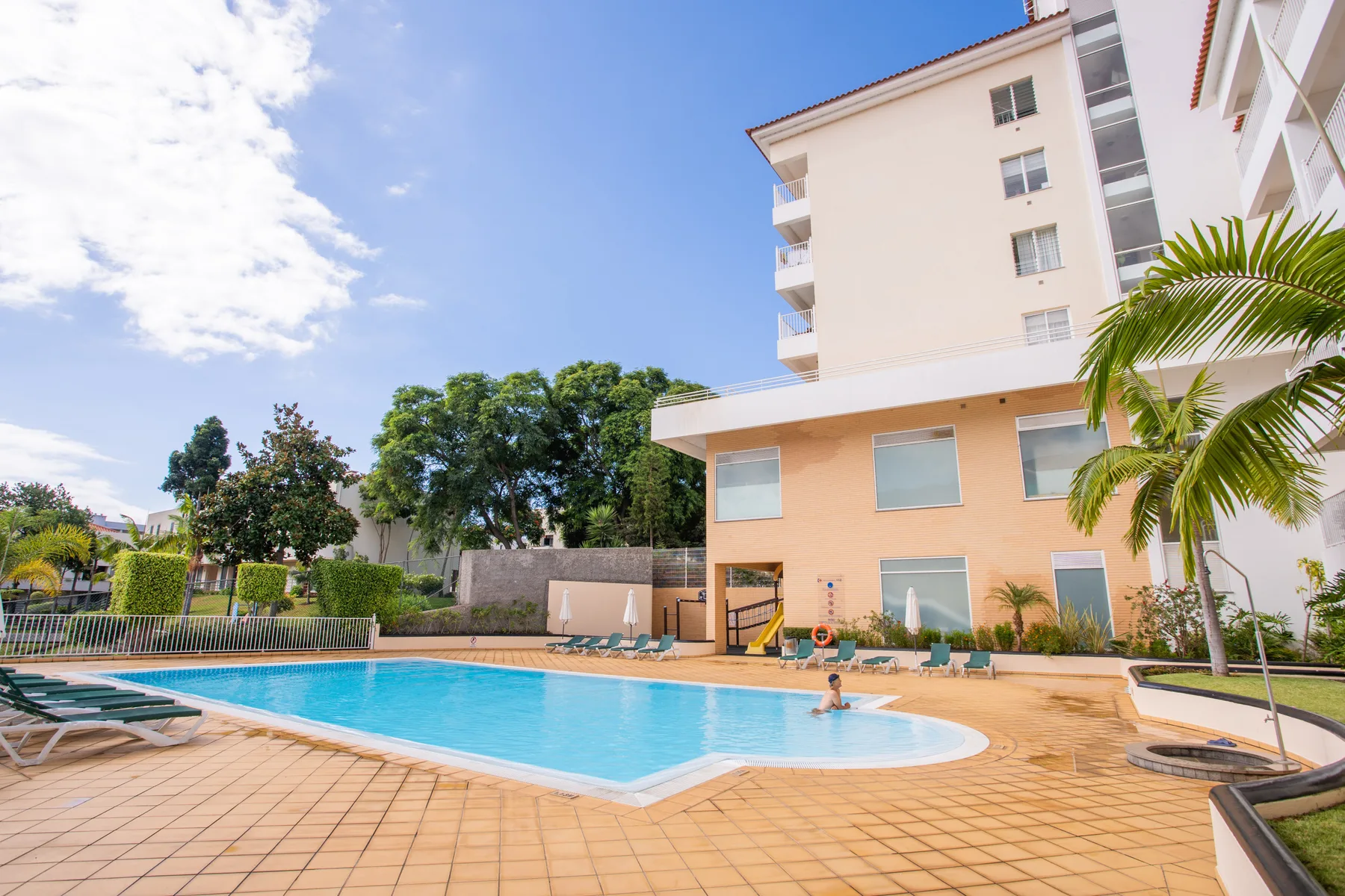 Outdoor swimming pool beside a modern apartment building, with loungers around the pool.
