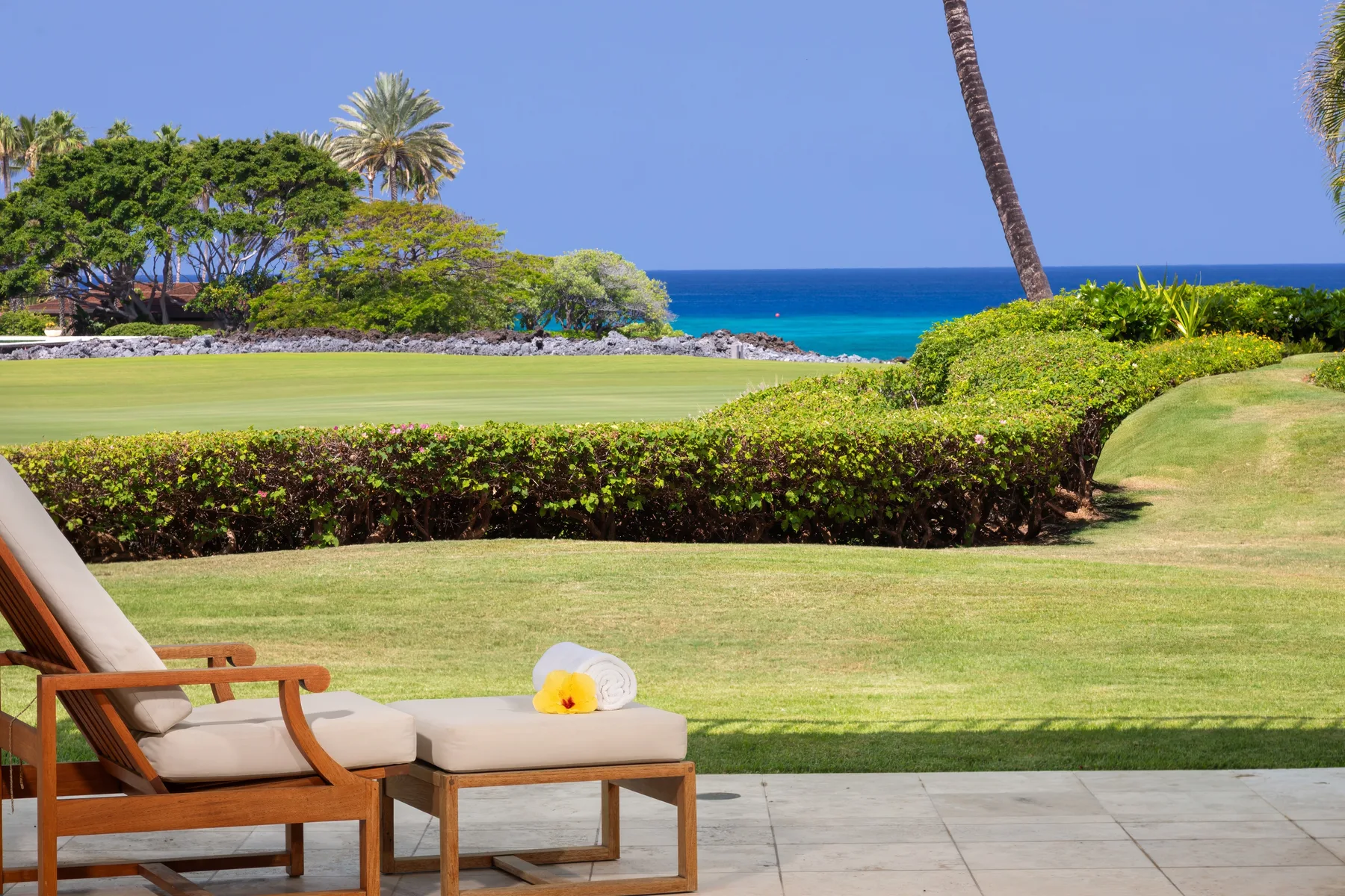 Outdoor seating overlooks a manicured lawn, greenery, and the ocean.